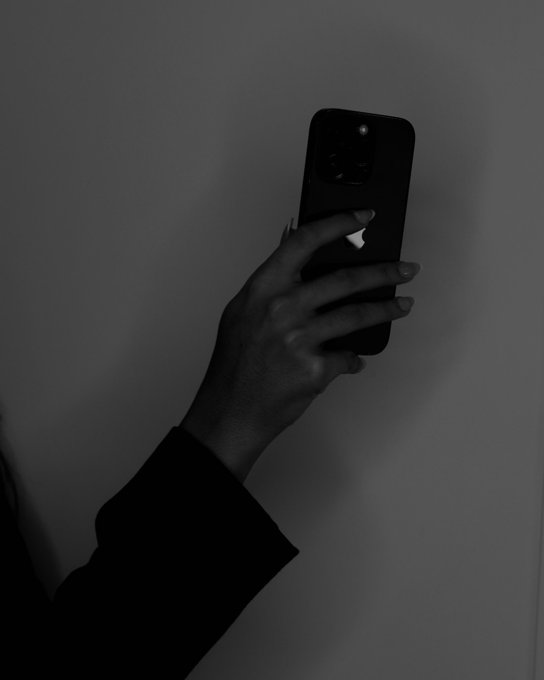 A person holding a smartphone and taking a photo or video, with a plain background.