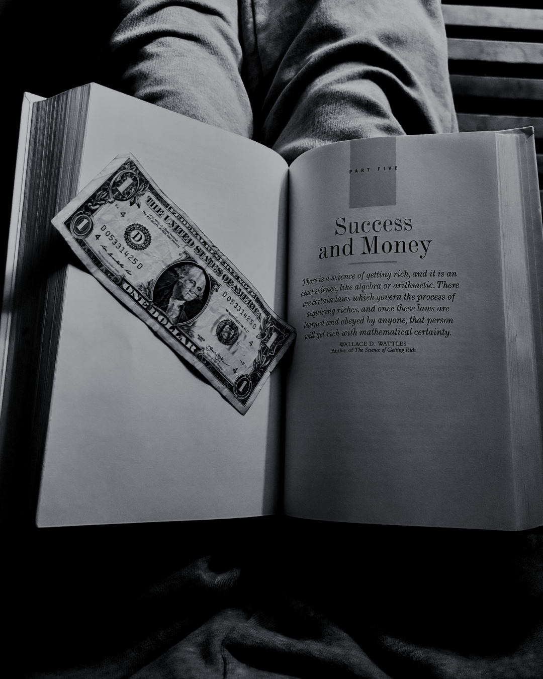 A person holds an open book titled 'Success and Money' with a one-dollar bill placed on the left page.