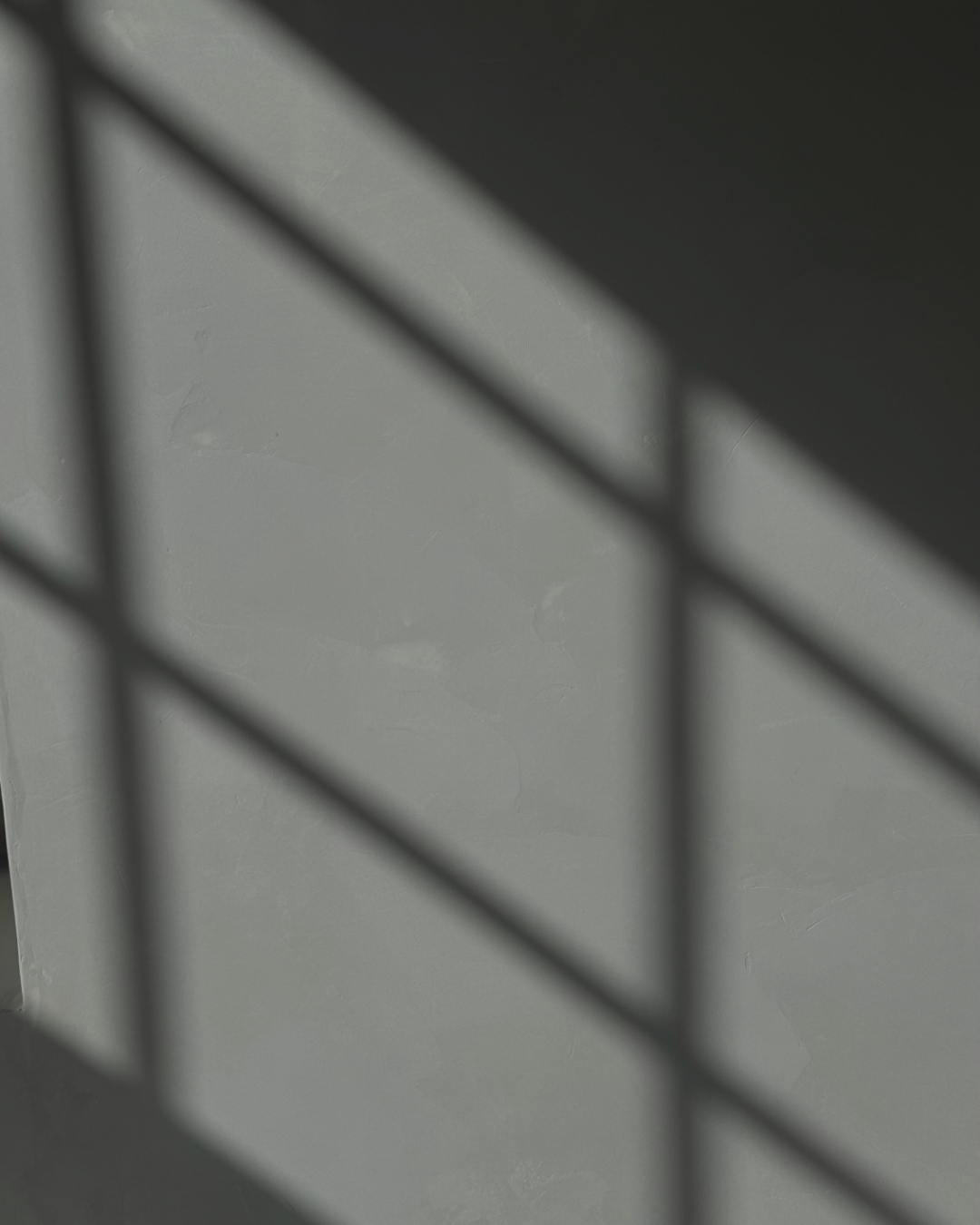 Close-up of a black metal grid casting a shadow on a light gray wall.