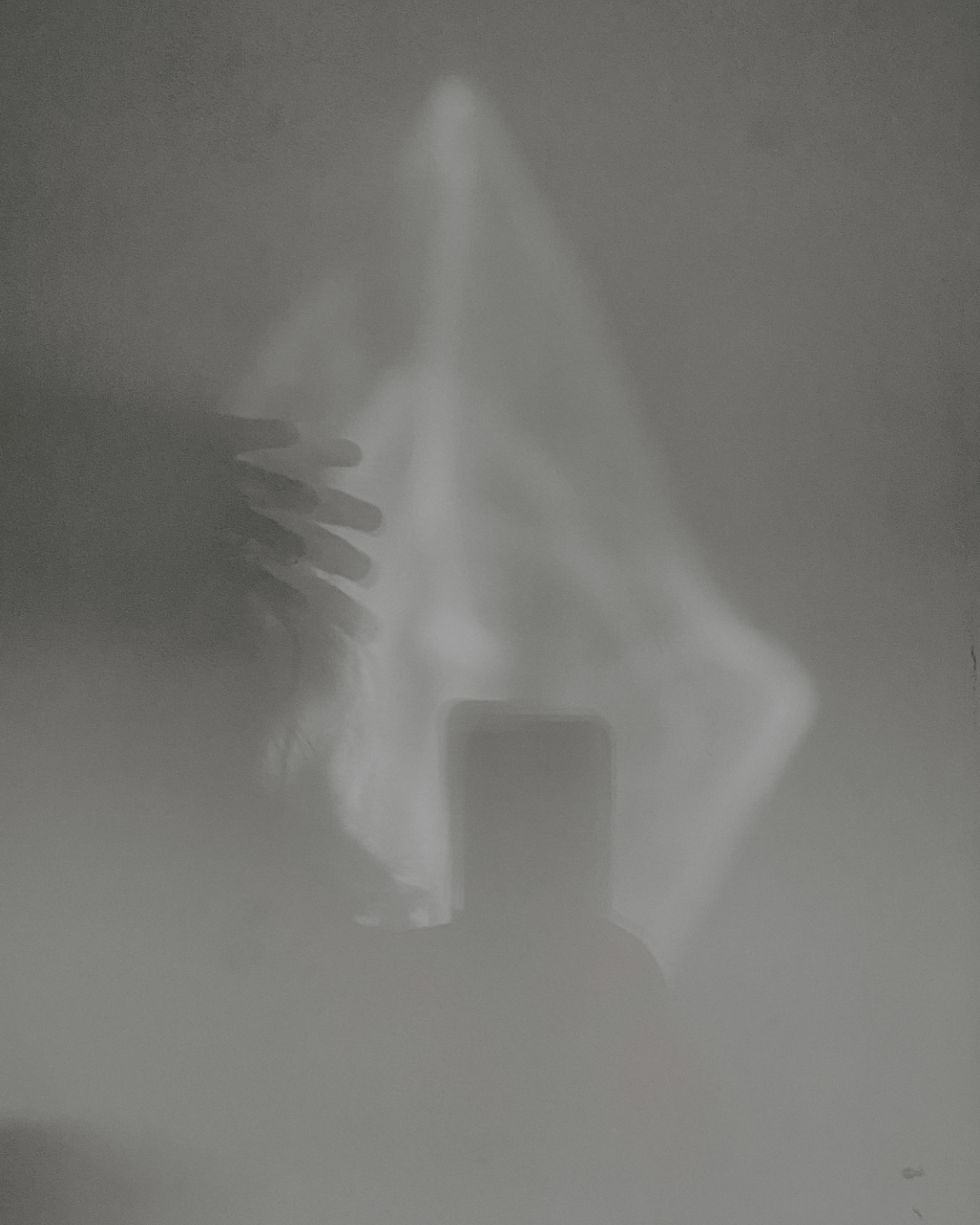 A hand holding a smartphone, capturing a reflection on a foggy, cloudy surface with a light source above creating a star-shaped pattern.