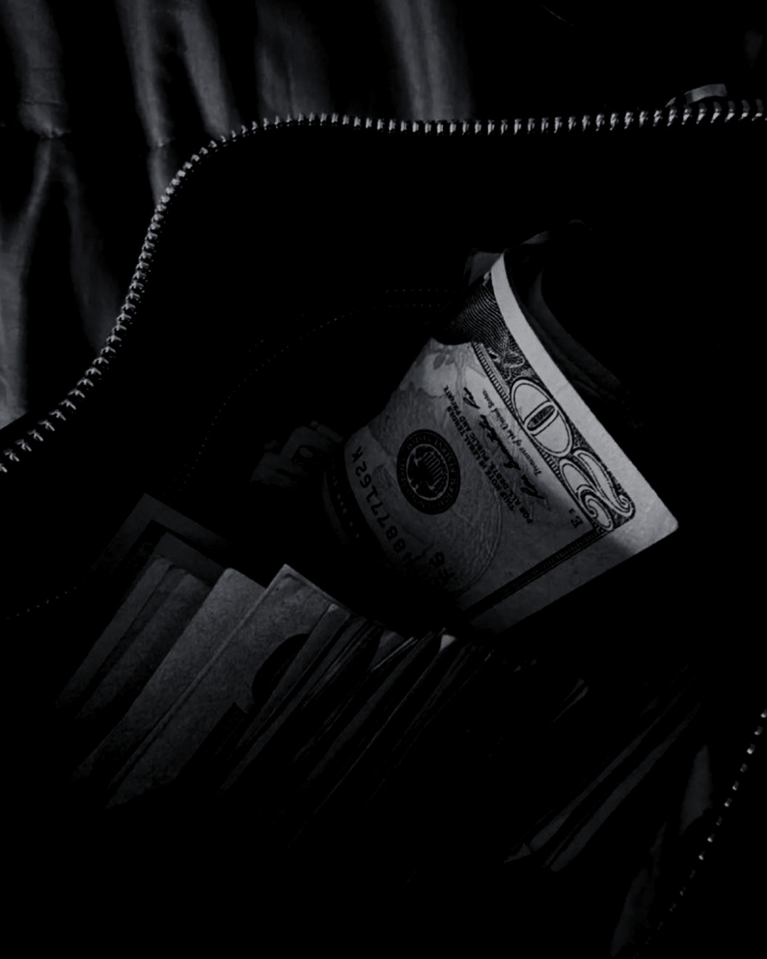 A partially open black bag containing a rolled-up twenty-dollar bill and some cards or photos.