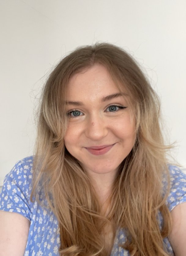 Smiling person with long hair wearing a patterned blue top, against a neutral background.