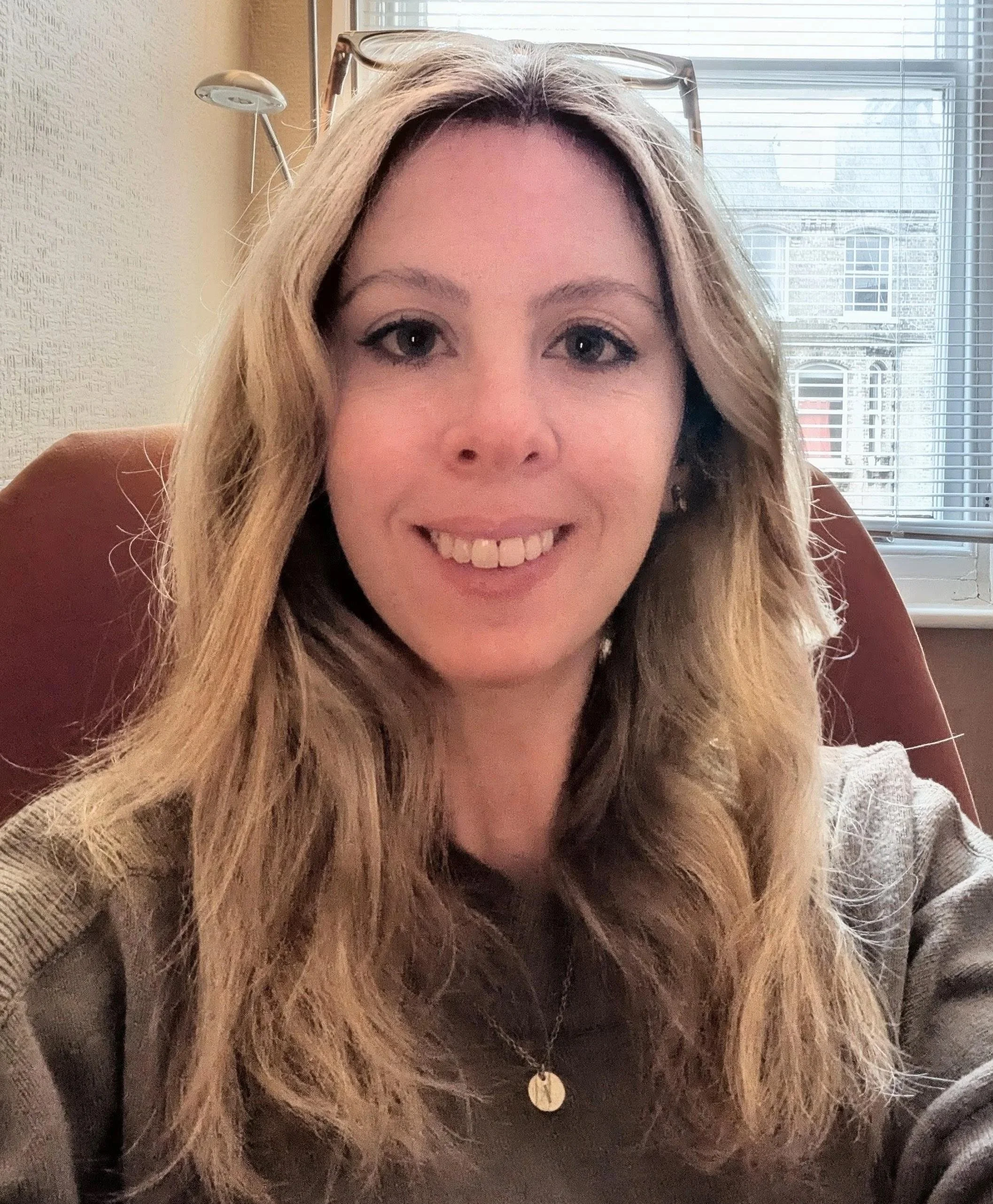 Person with blonde hair and floral top smiling against a white background.