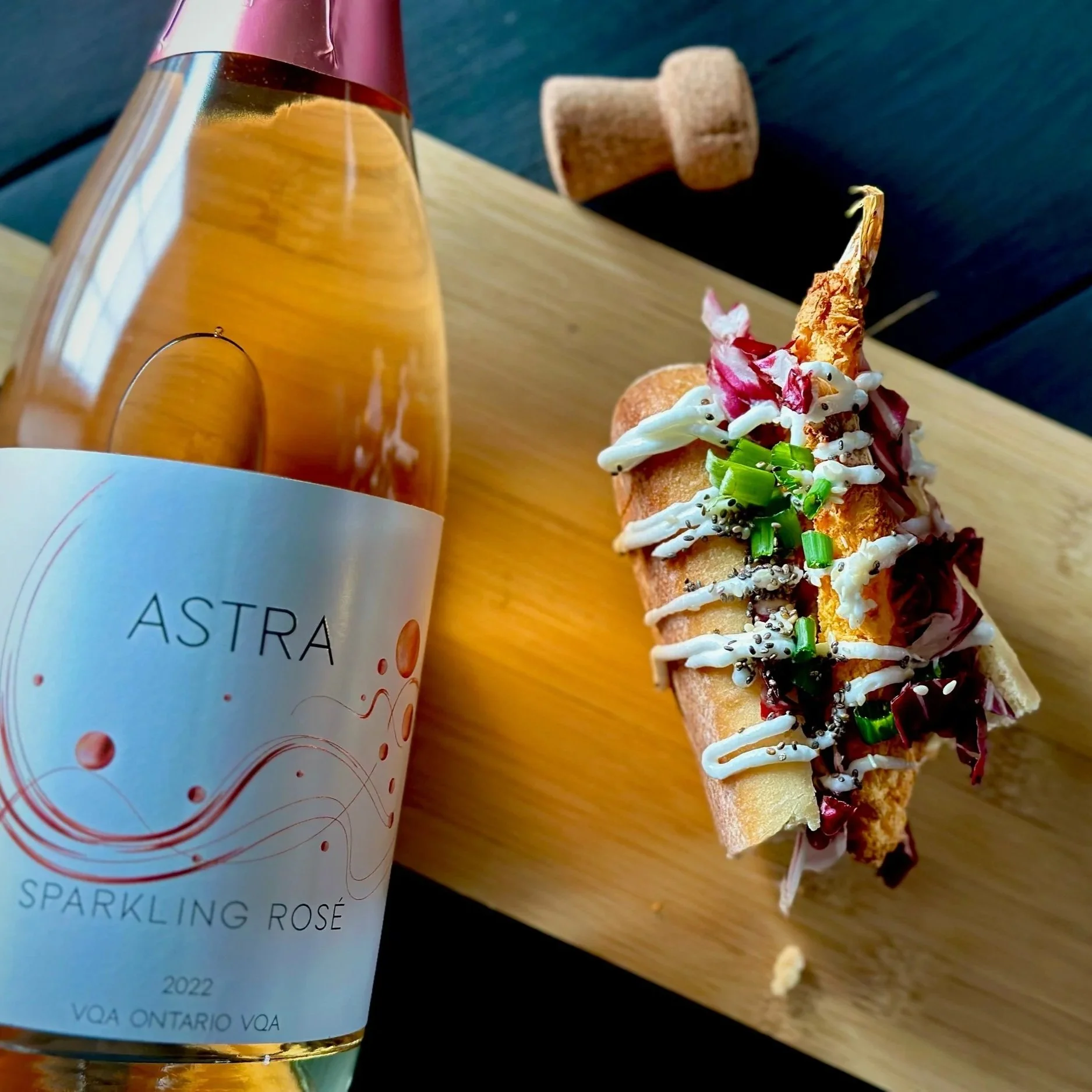 A glass of Riverview Cellars Icewine next to a beef slider topped with blue cheese on a white plate, set on a wooden crate in an indoor event space