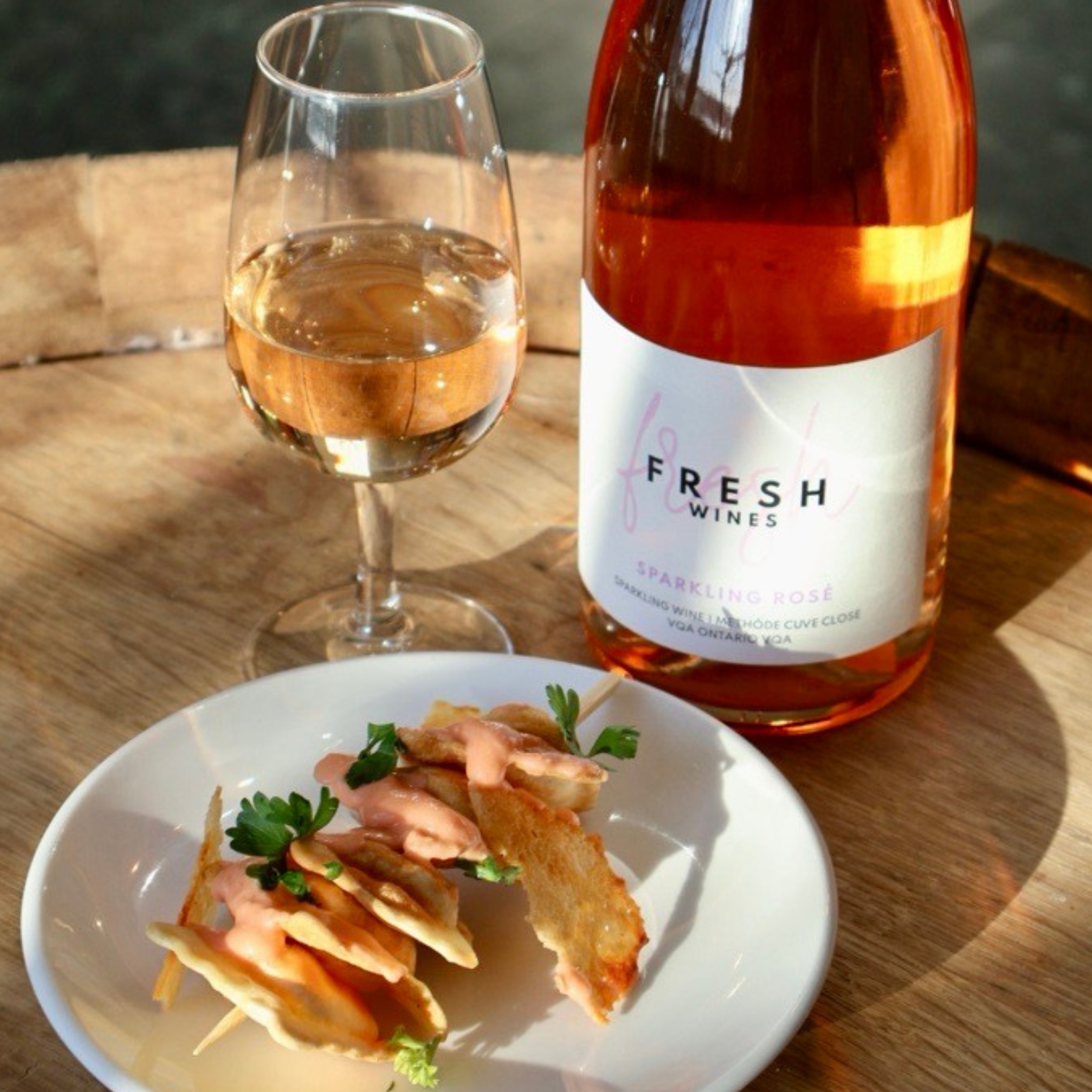 Fresh Wines Vidal Icewine bottle paired with a dessert plate featuring a crumble-topped fruit dish, a dollop of whipped cream, and a strawberry, set on a rustic wooden surface.