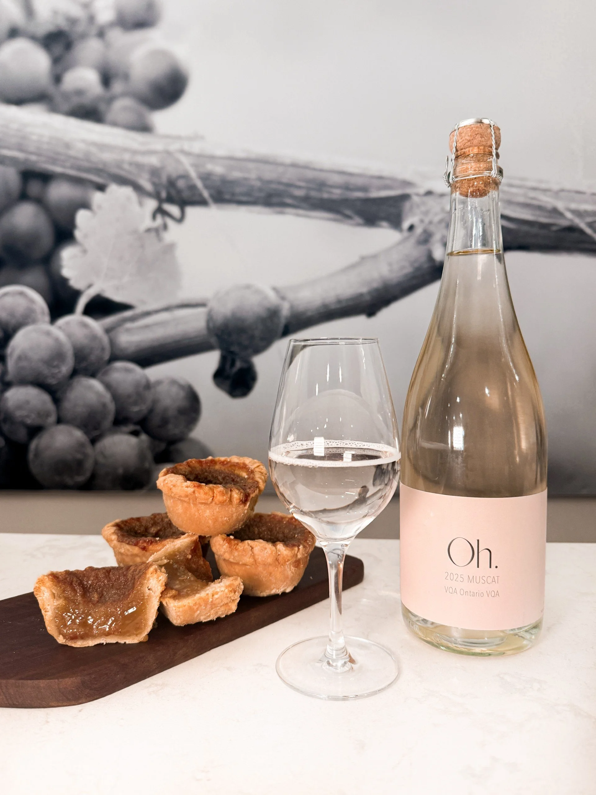 A bottle of Marynissen Sparkling Vidal Icewine with a glass of the wine and a pulled pork slider on a wooden board.