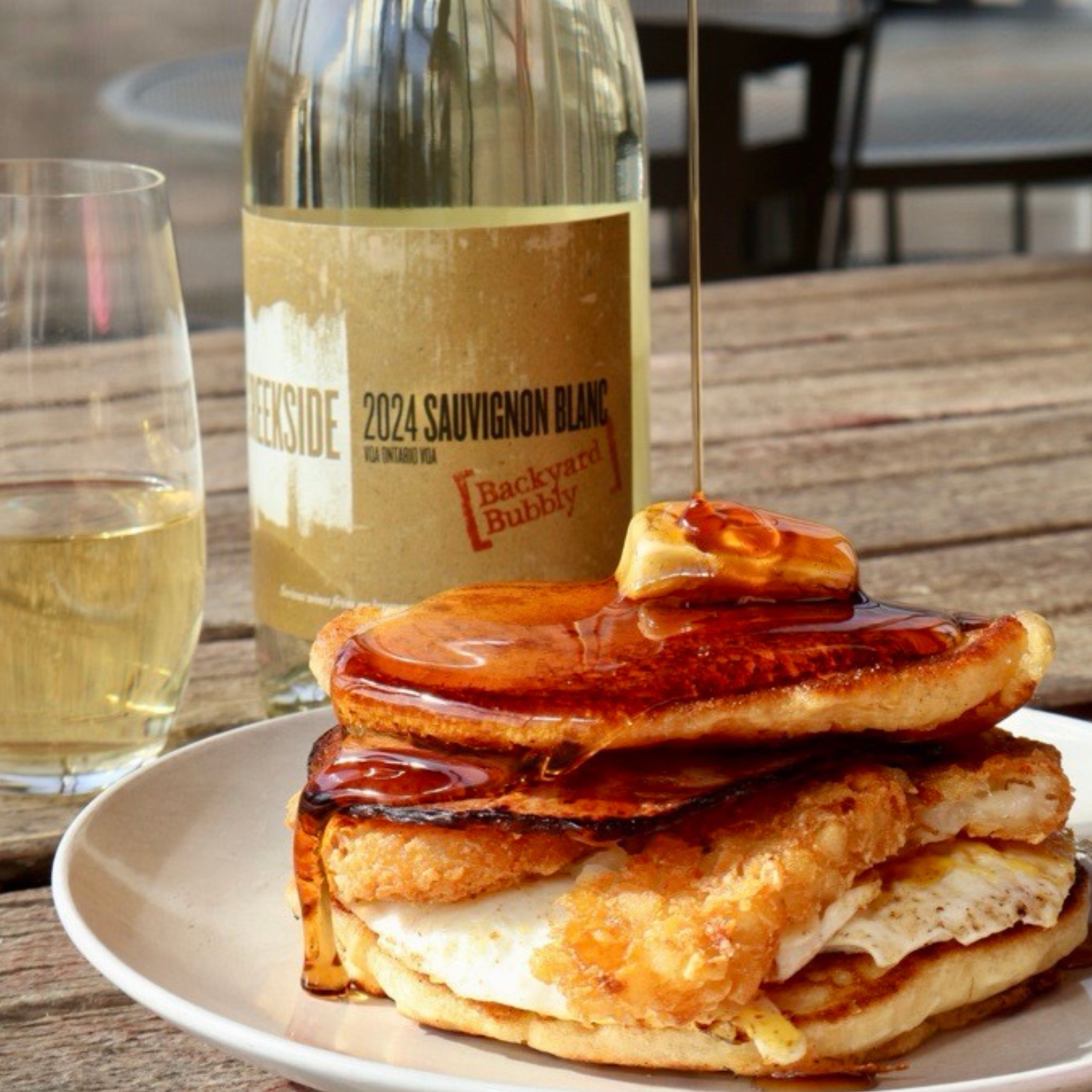 Creekside Cabernet Sauvignon Icewine bottle next to a glass of icewine and a plate with a dessert topped with strawberries and whipped cream, set outdoors with a scenic, wooded background
