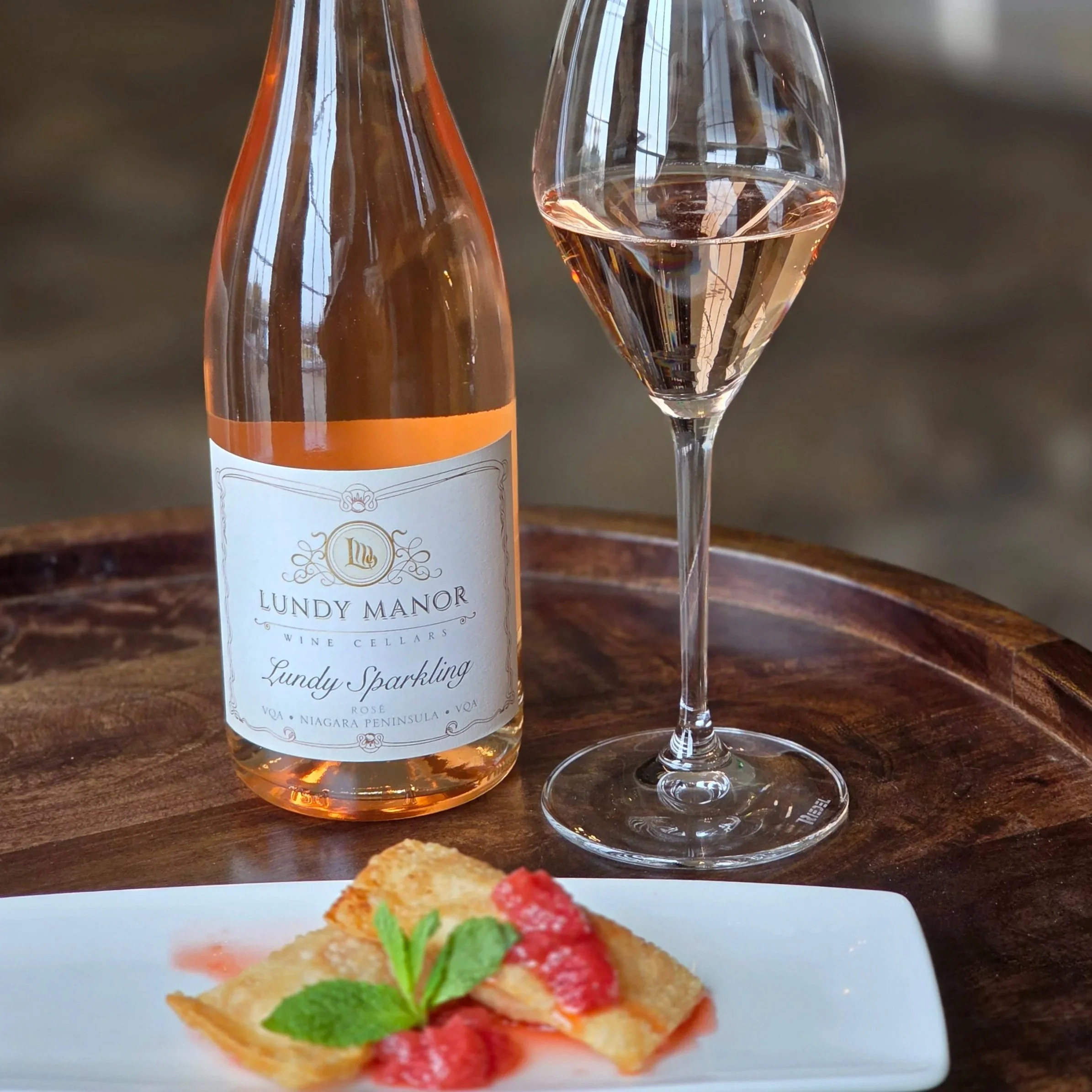 A bottle of Malivoire Icewine with a glass of the wine and a caramelized onion tart topped with bacon, crème fraîche, and shredded cheese on a white plate.