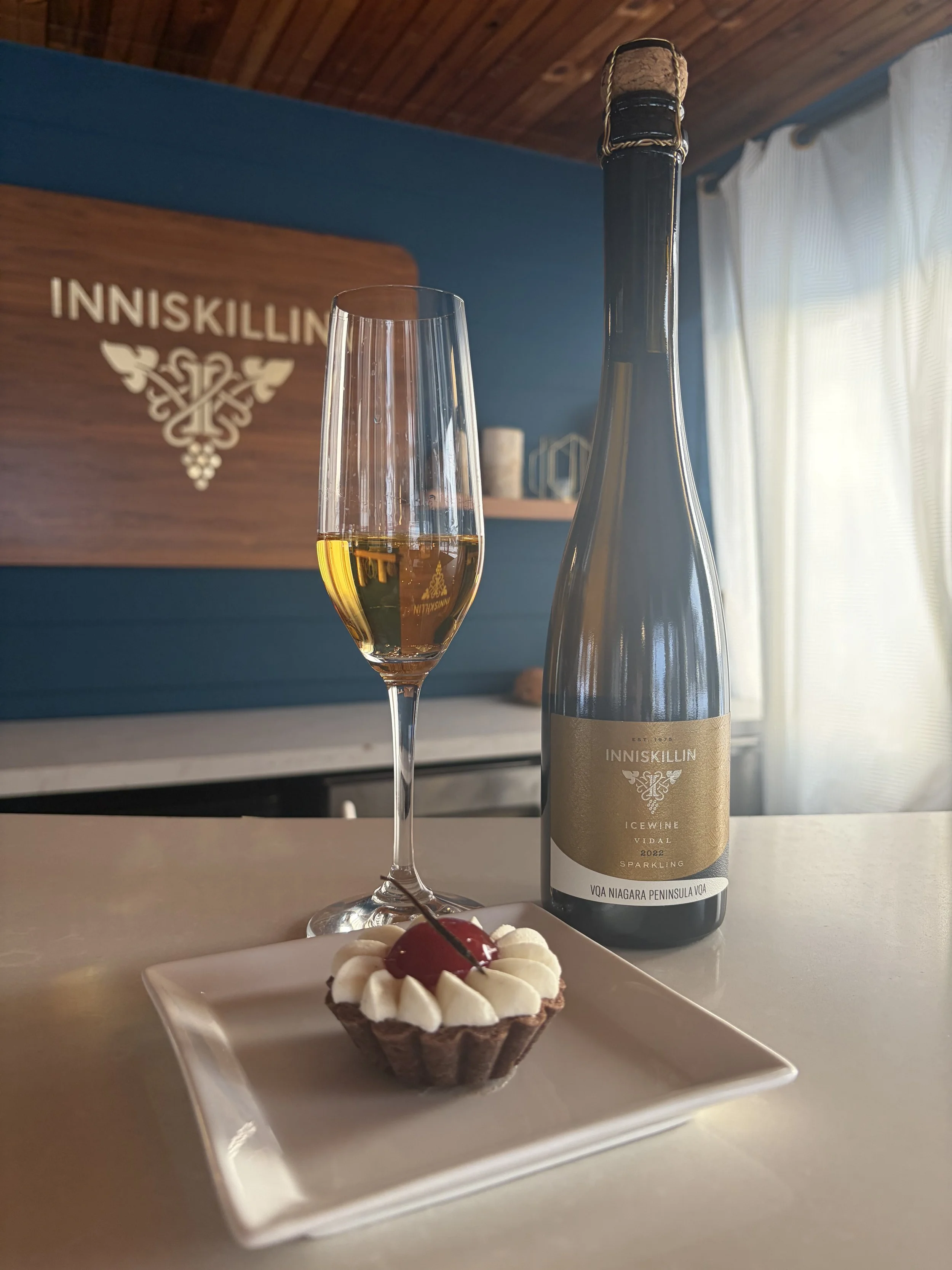 A bottle of Inniskillin Vidal Sparkling Icewine with a filled glass, paired with crispy chicken, waffles, and dipping sauces on a wooden board.