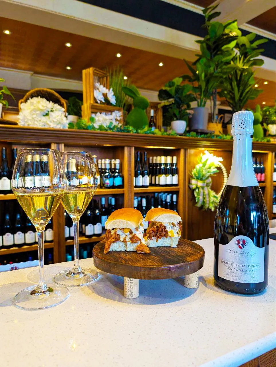 Two bottles of Reif Estate Vidal Icewine with glasses of the wine, paired with a roasted pork sandwich on a small wooden stand