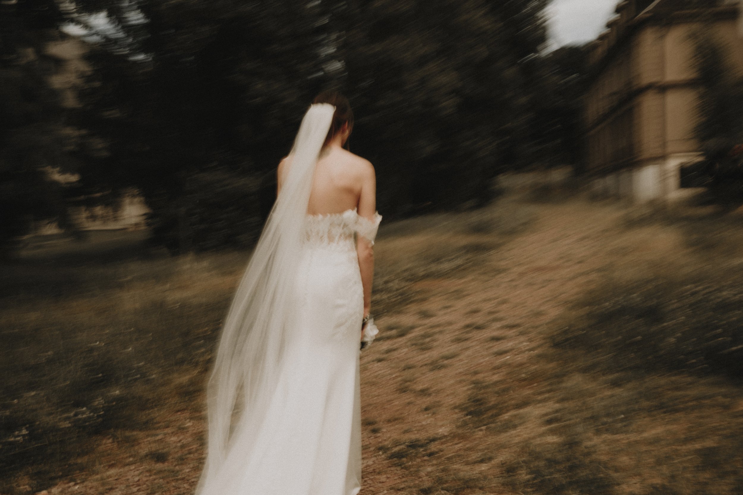 Mariée vue de dos avec une robe blanche et un voile, marchant en extérieur.