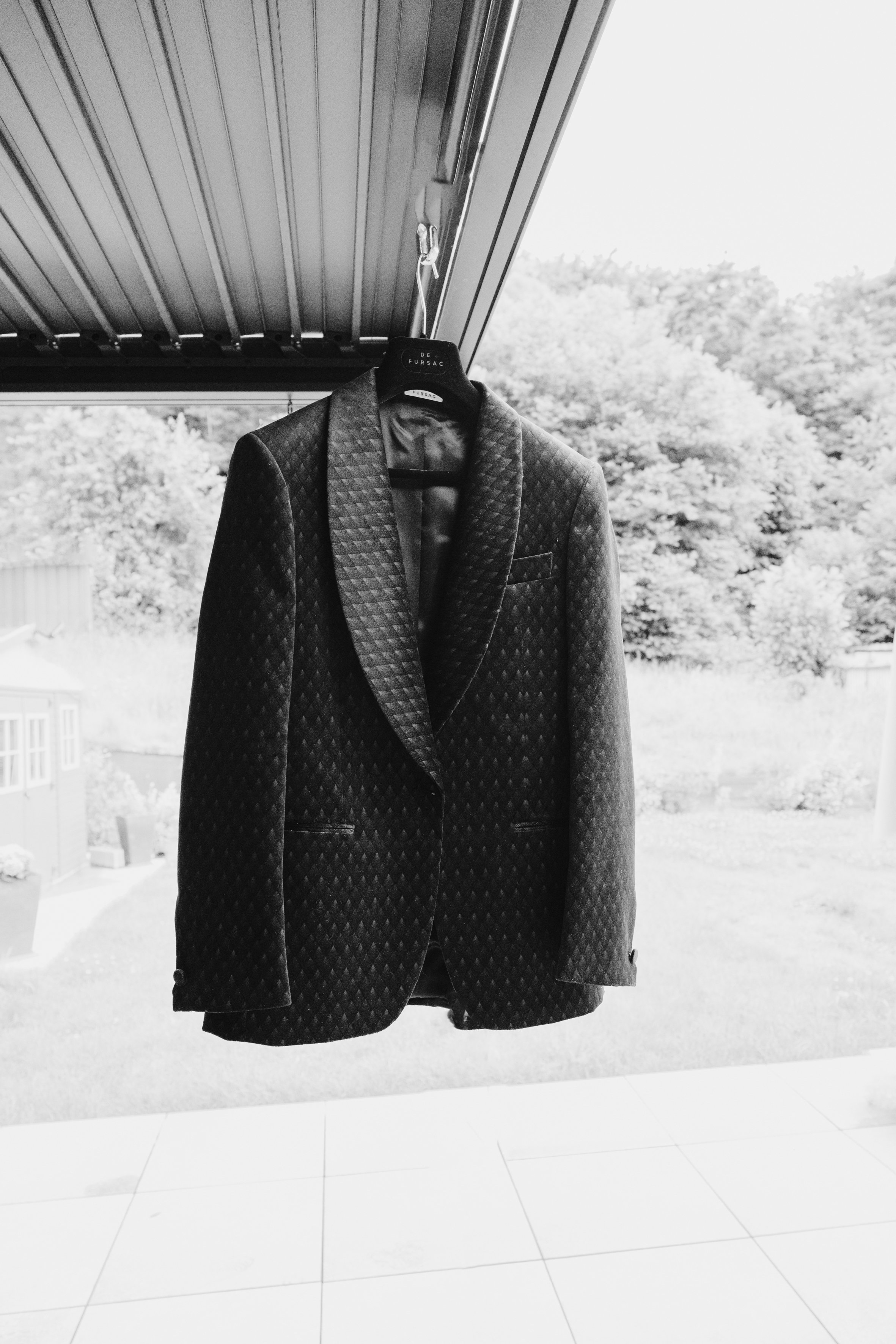 Veste de costume sombre suspendue sous un toit, fond extérieur flou.