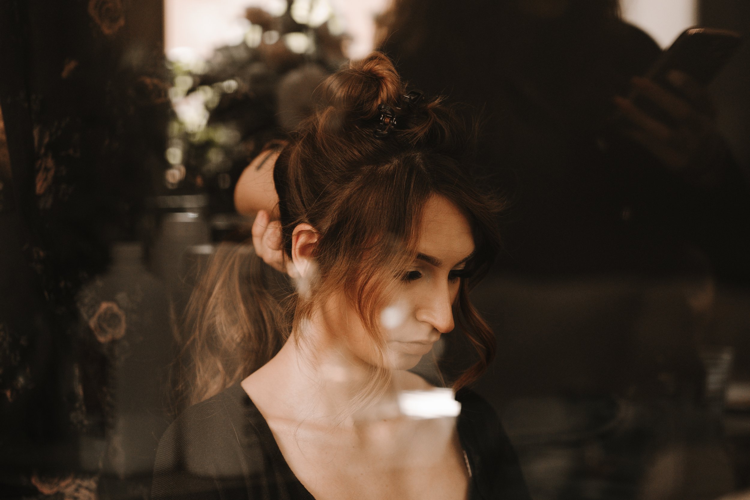 Femme aux cheveux relevés en cours de coiffure, reflet devant une vitre, fond flou.