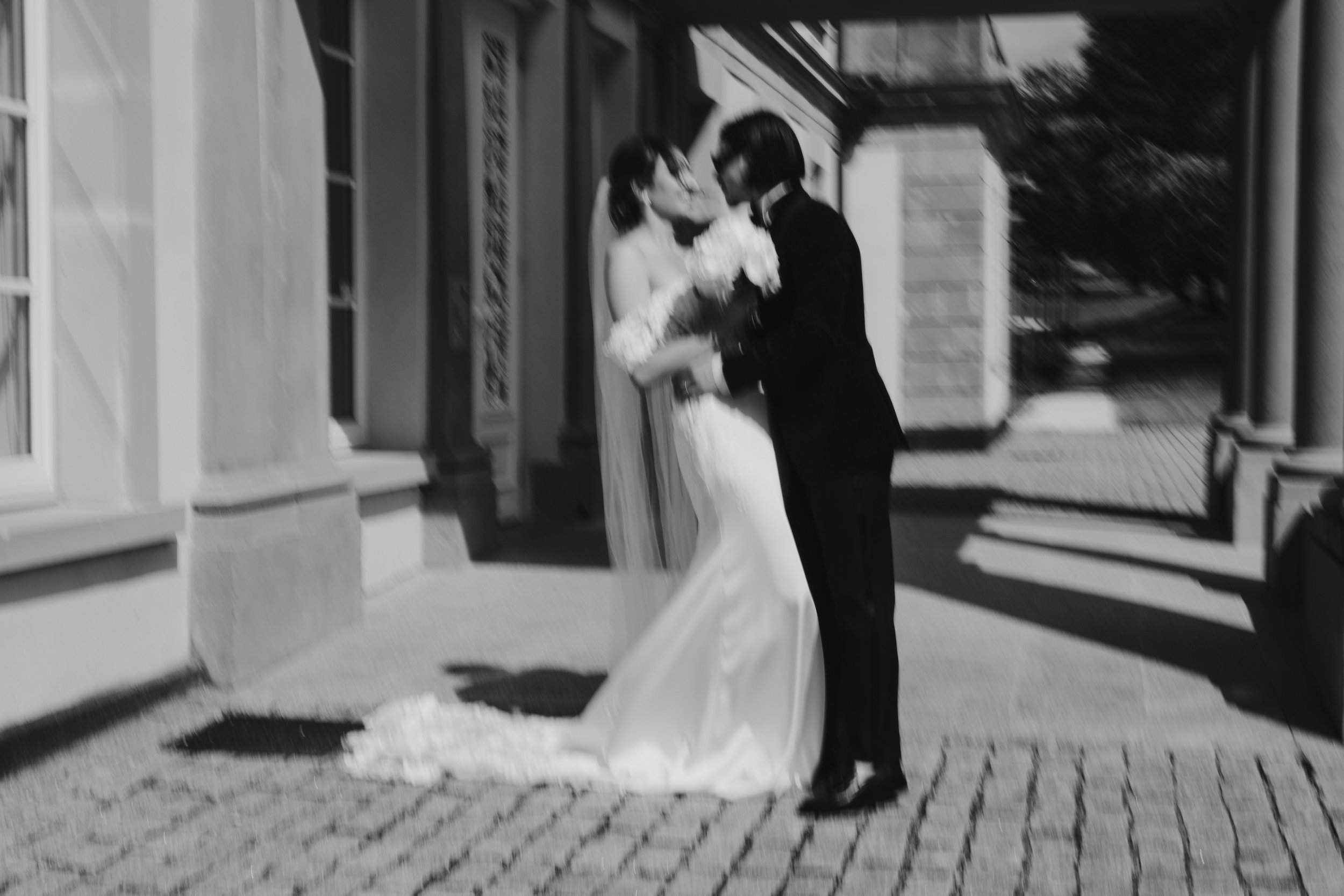 Image floue d'un couple en tenue de mariage s'embrassant devant un bâtiment.