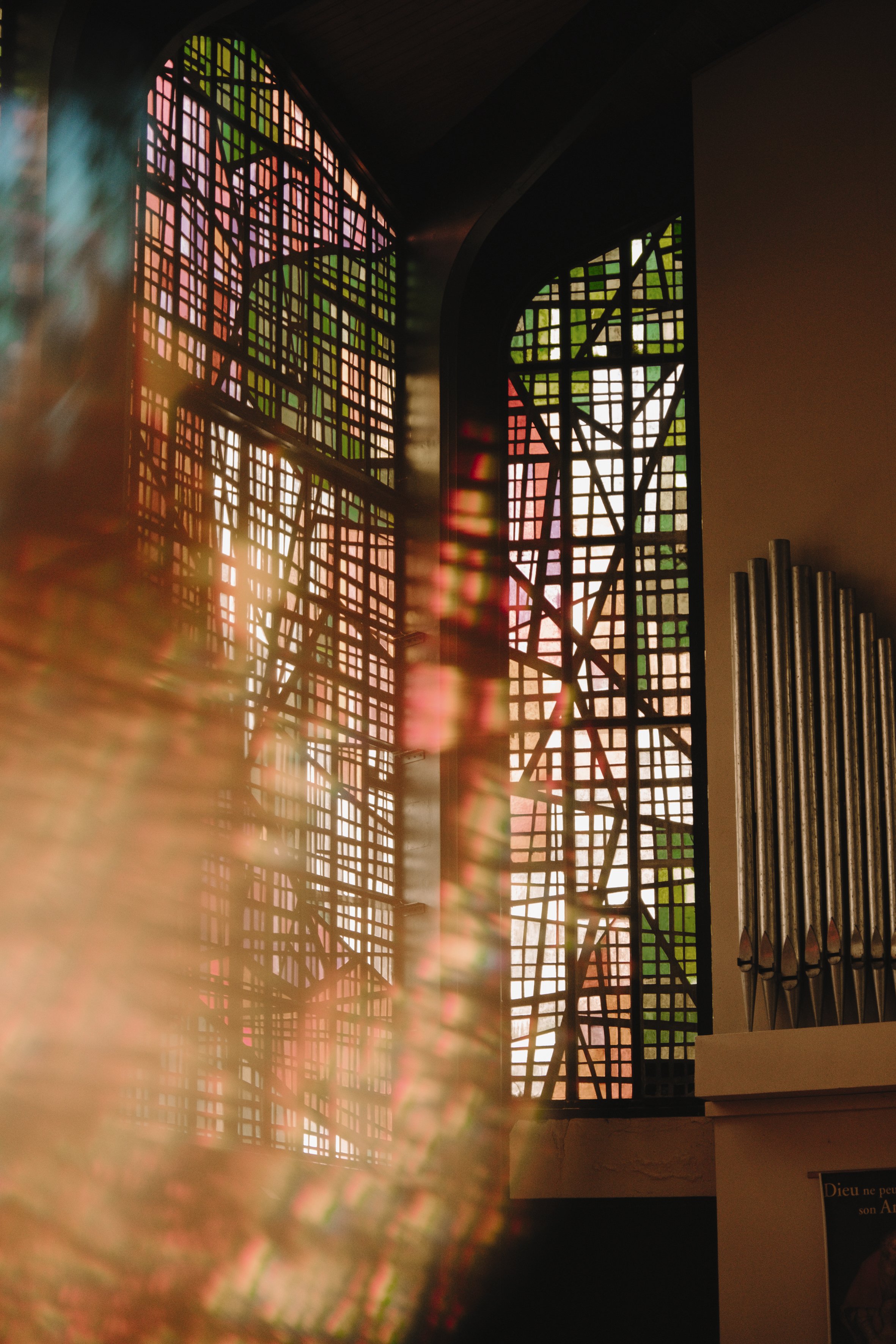 Vitraux colorés dans une église avec des motifs géométriques. Lumière filtrée à travers les vitraux et des tuyaux d'orgue visibles à droite.