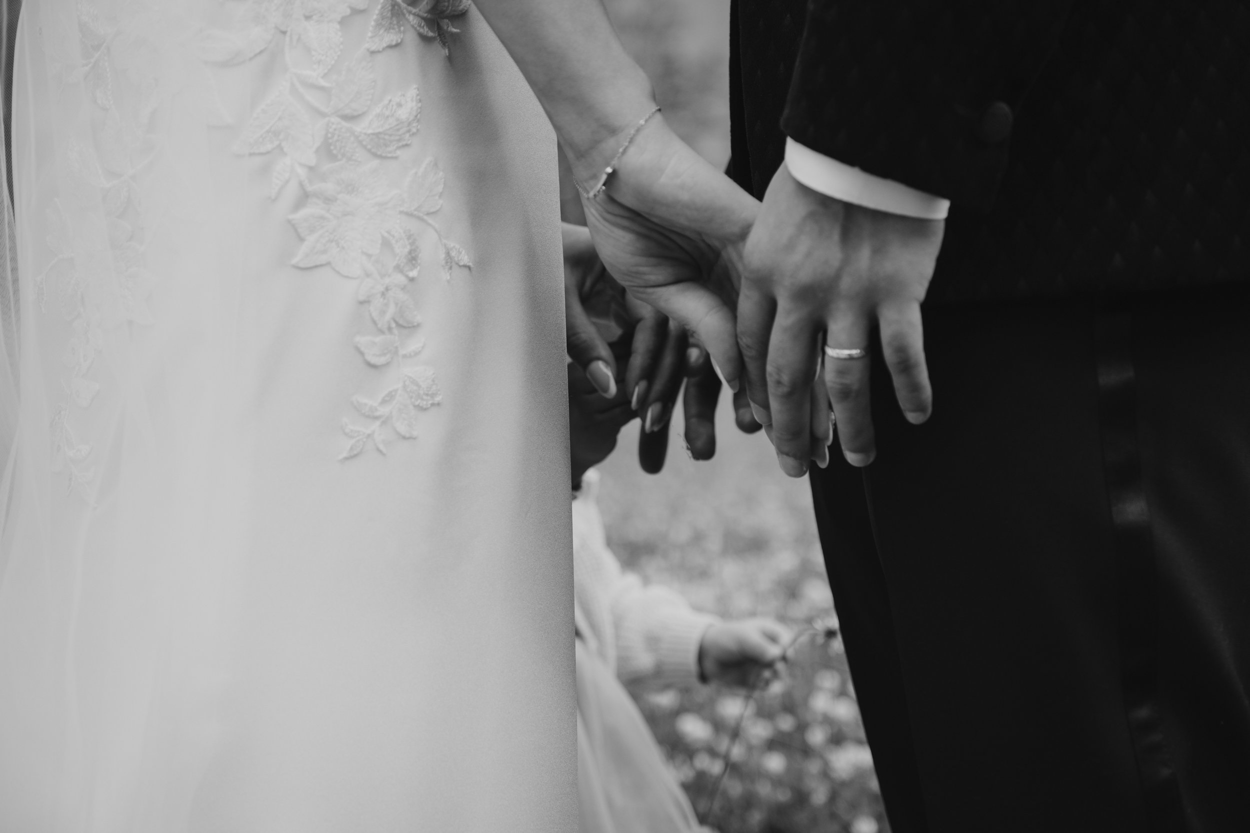 Un couple tenant la main d'un enfant. La femme porte une robe de mariée avec des motifs floraux et l'homme porte un costume sombre.