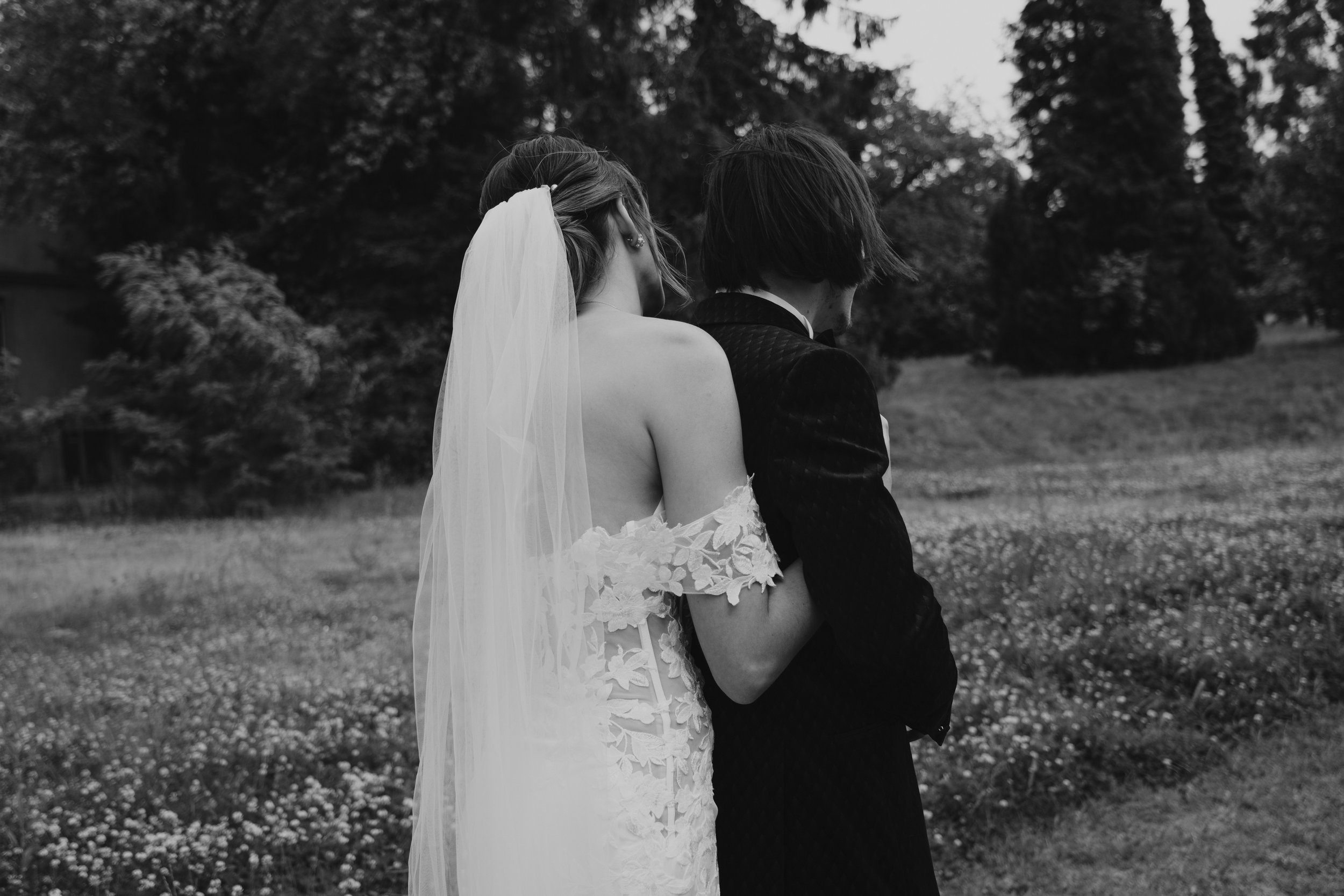 Un couple de dos, vêtu de vêtements de mariage, dans un champ avec des arbres en arrière-plan.