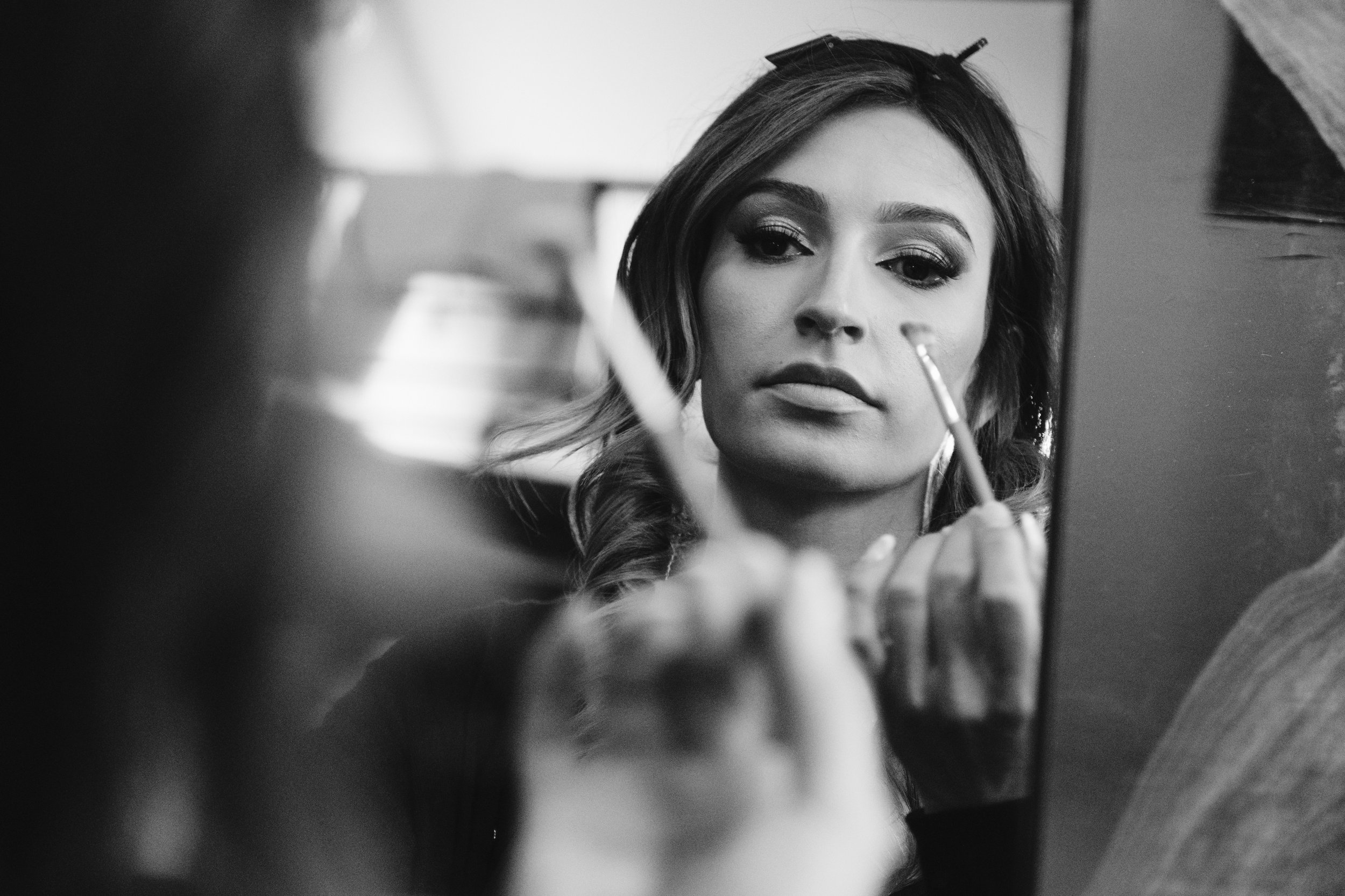 Une femme se maquillant devant un miroir, tenant un pinceau de maquillage.