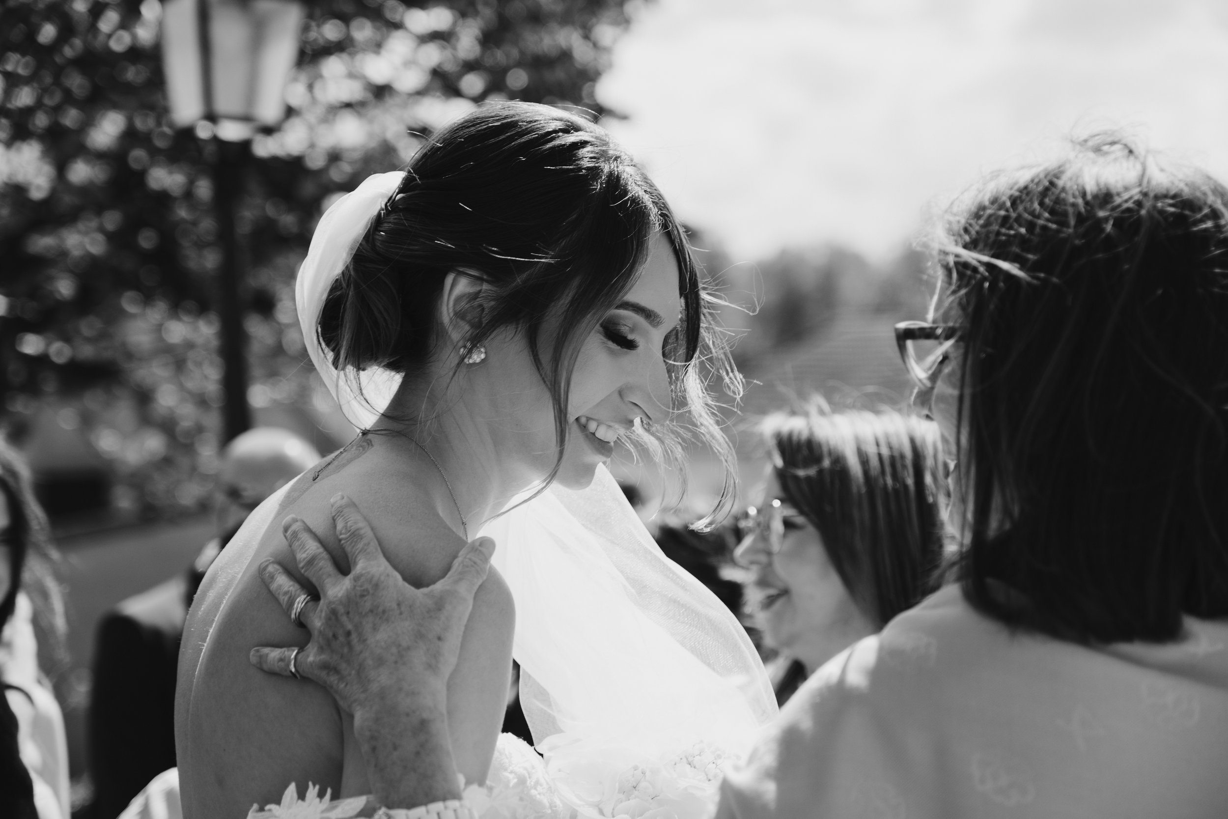 Photographie en noir et blanc d'une mariée souriante avec une femme mettant la main sur son épaule.
