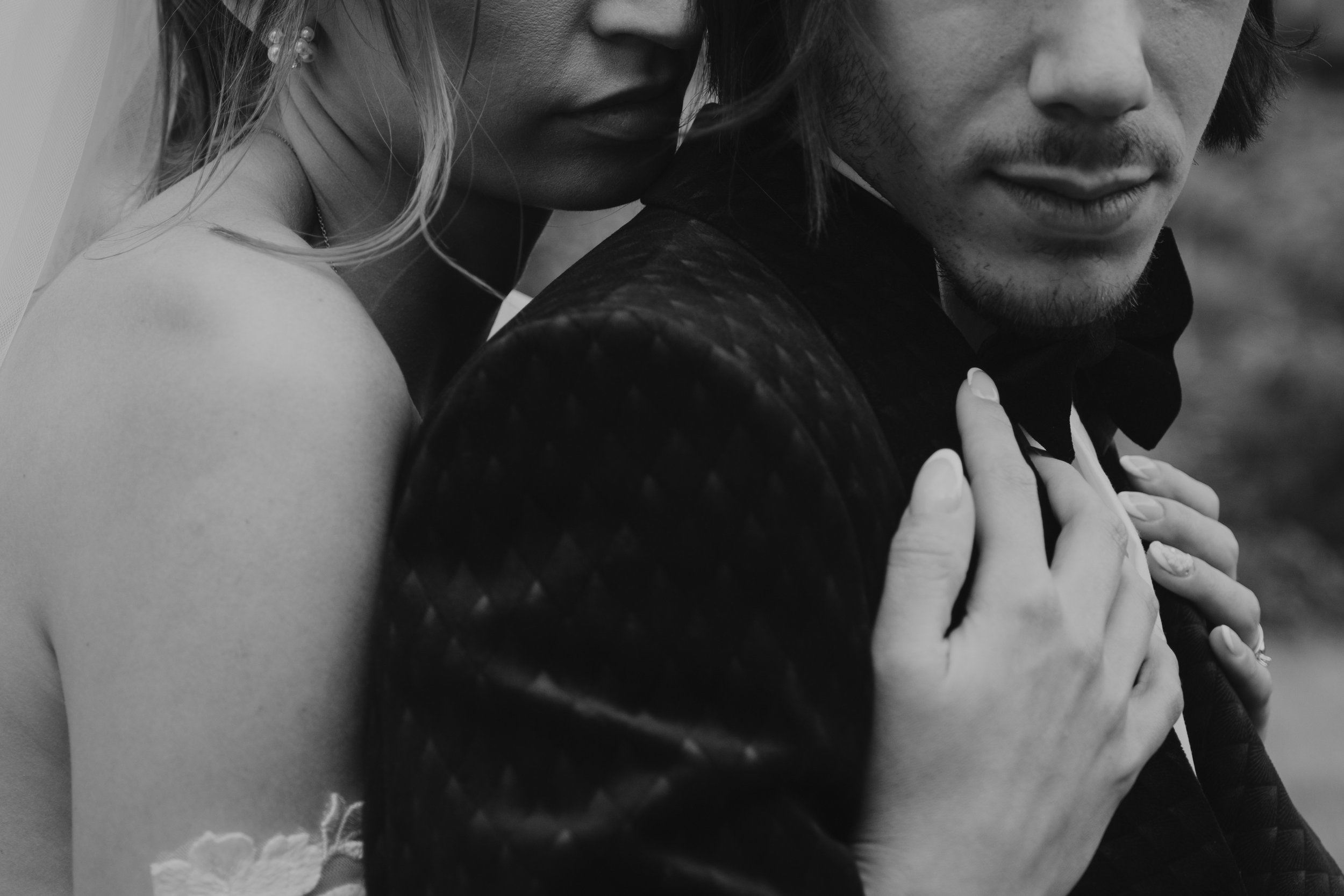 Un couple en tenue de mariage en noir et blanc, en train de s'enlacer.