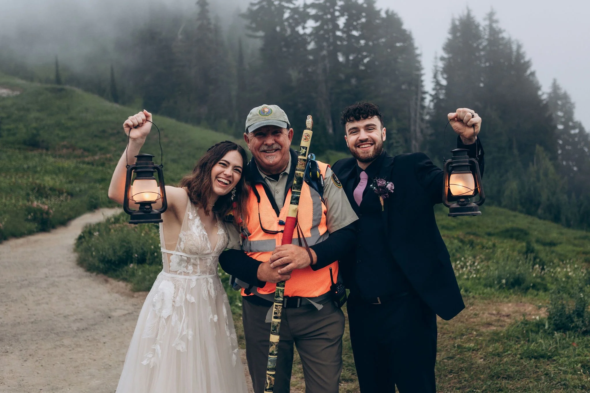Eloping couple posing with a Mount Rainier National Park ranger at Paradise while holding lanterns on a foggy trail