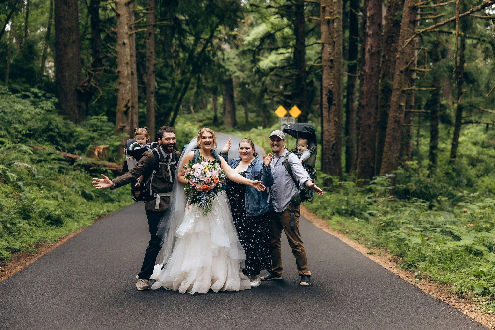 Intimate wedding celebration in Oregon with the couple surrounded by family and young children, standing together on a forest road