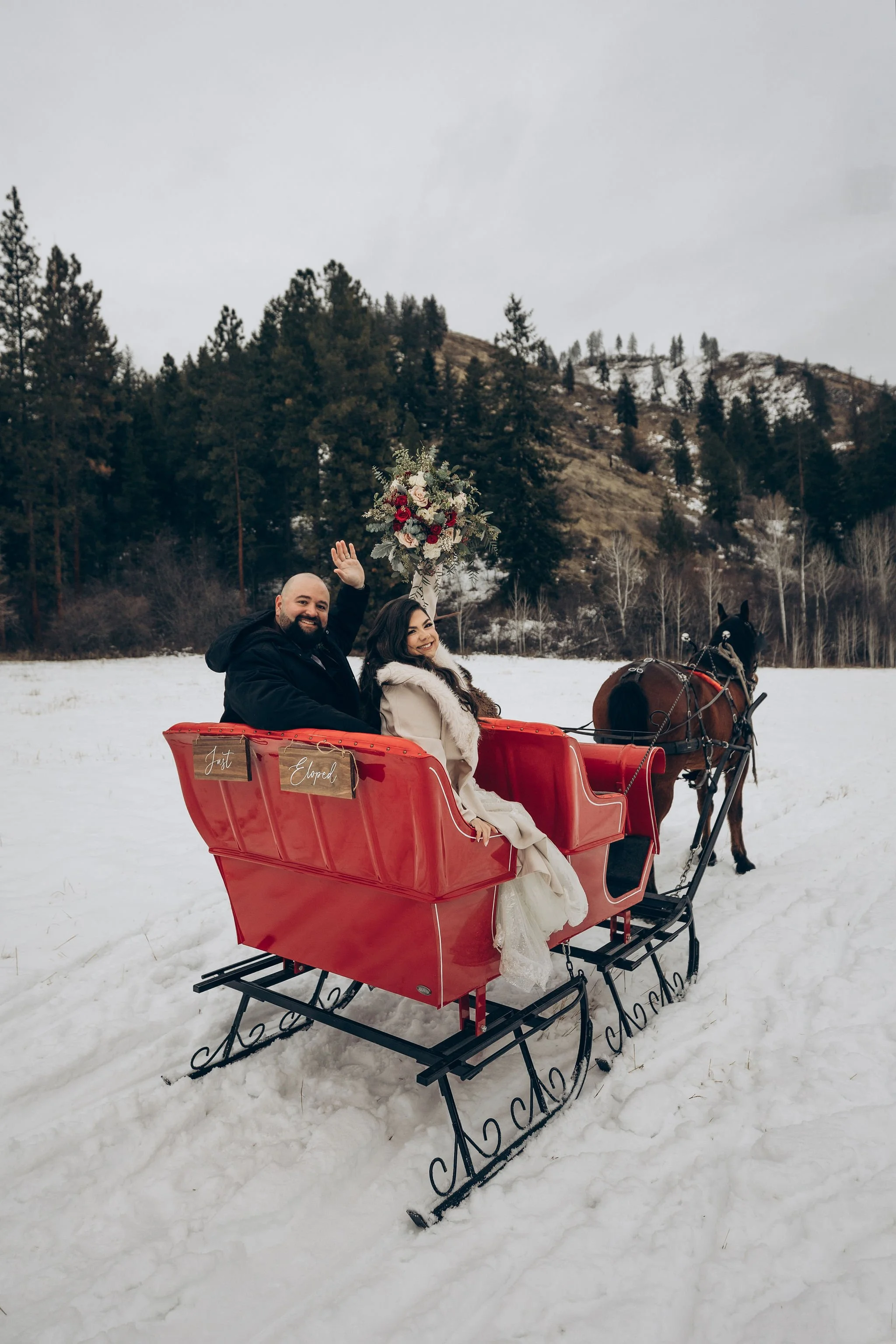 Couple riding in a red sleigh with a “Just Eloped” sign during a winter wedding in Leavenworth, Washington
