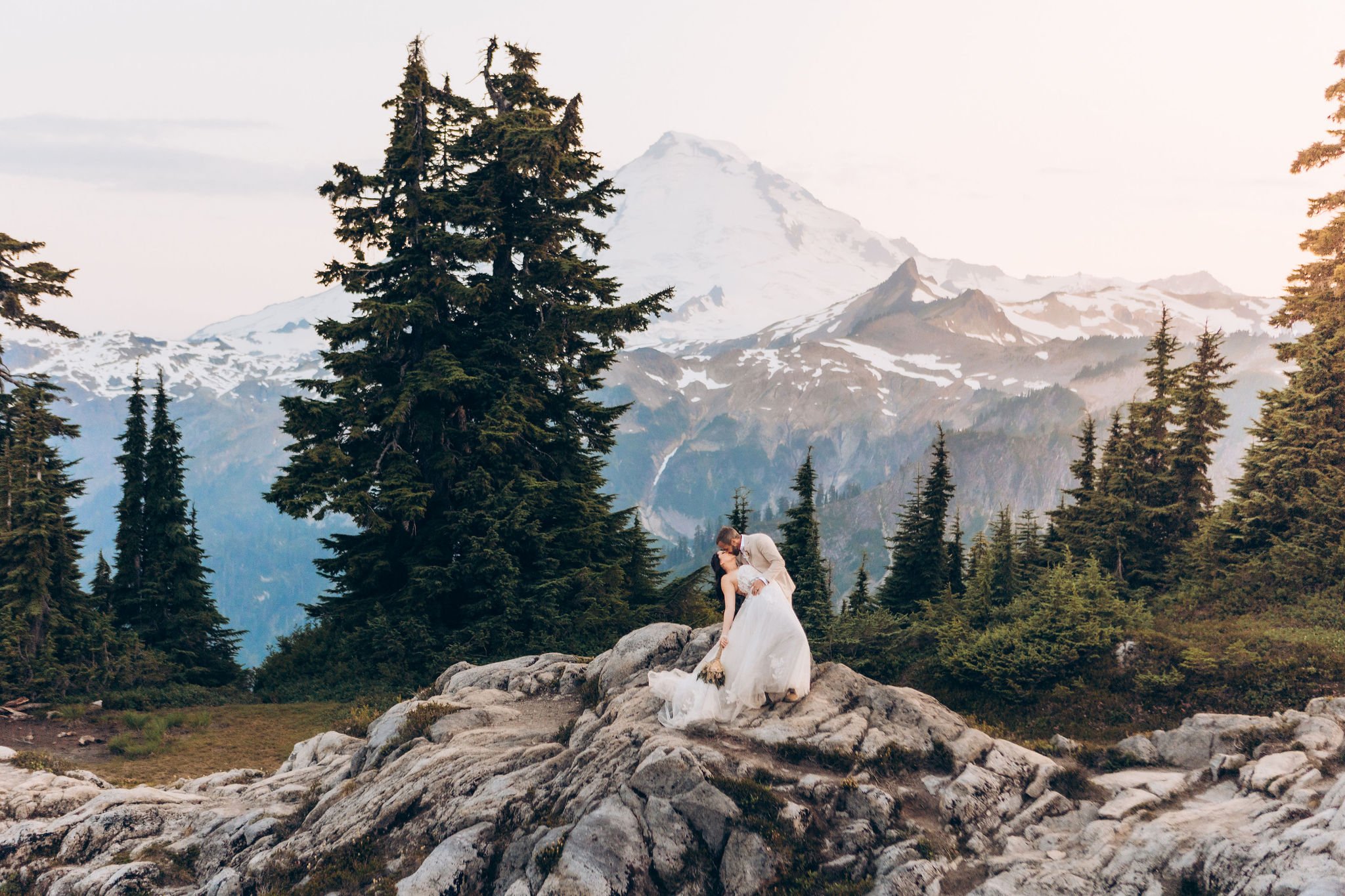 Couple embracing during a Mt Baker elopement on rocky overlook with Washington mountain landscape and evergreen forest