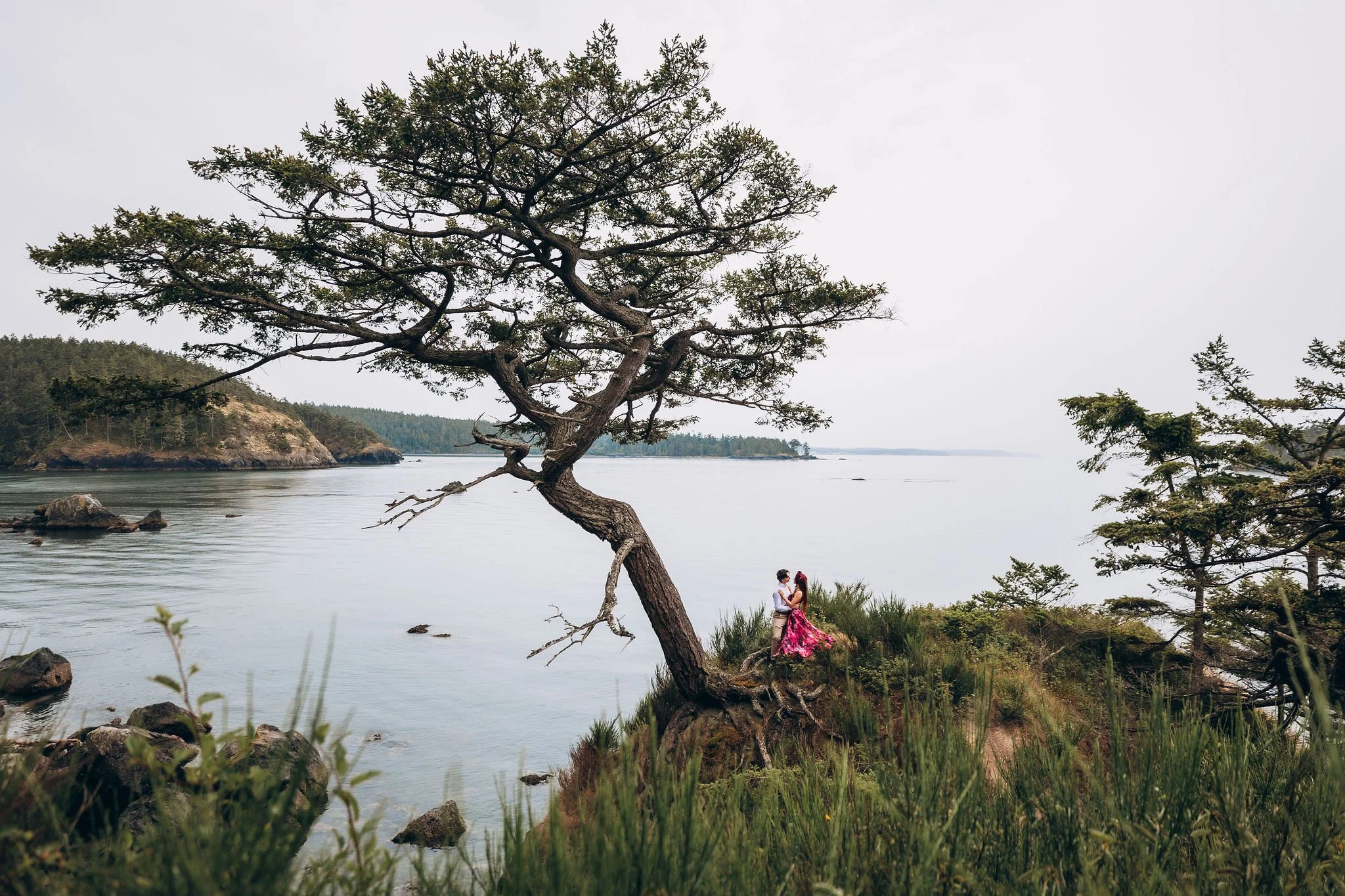 Couple embracing during a Deception Pass elopement on Whidbey Island with a red elopement dress and coastal views