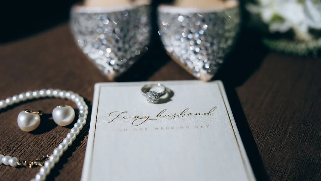 Wedding getting ready details featuring engagement ring, vow book, pearl jewelry, and bridal shoes laid out before the ceremony