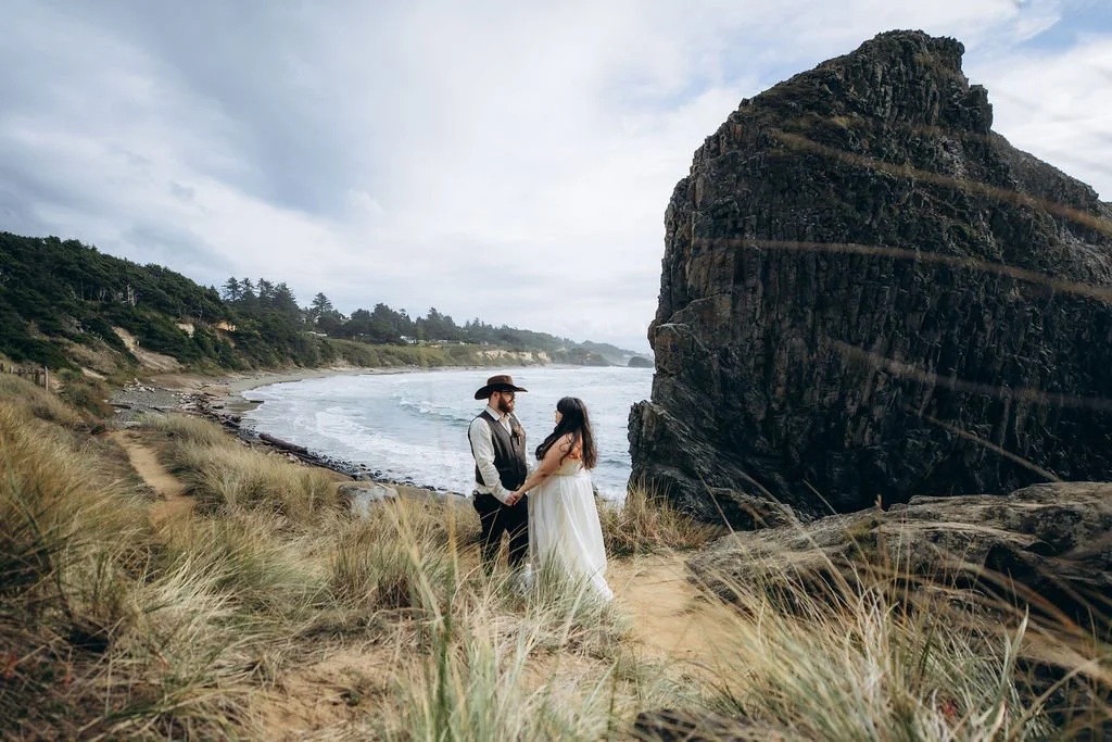 Couple holding hands during a fall elopement in Newport, Oregon, standing on a coastal cliff overlooking the ocean