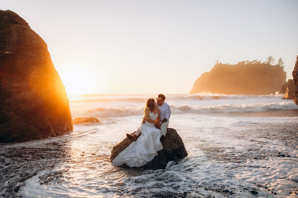 Ruby Beach elopement in Olympic National Park, with a couple sitting on a sea stack rock as waves roll in at sunset