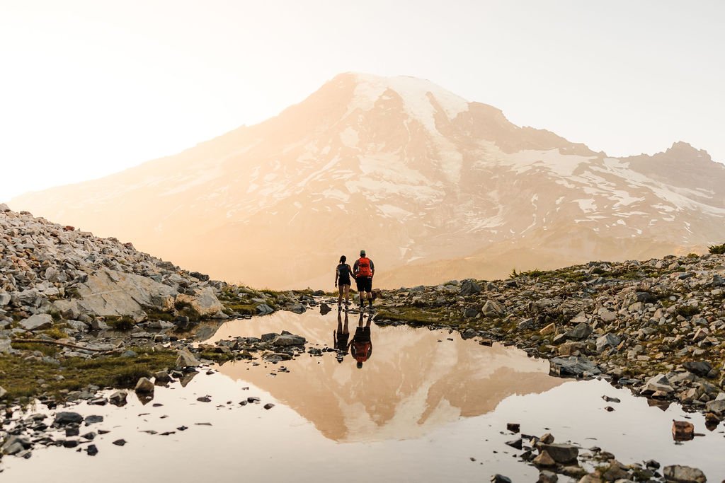 Mount Rainier elopement photo with a couple walking toward the mountain, reflected in an alpine tarn at sunset.
