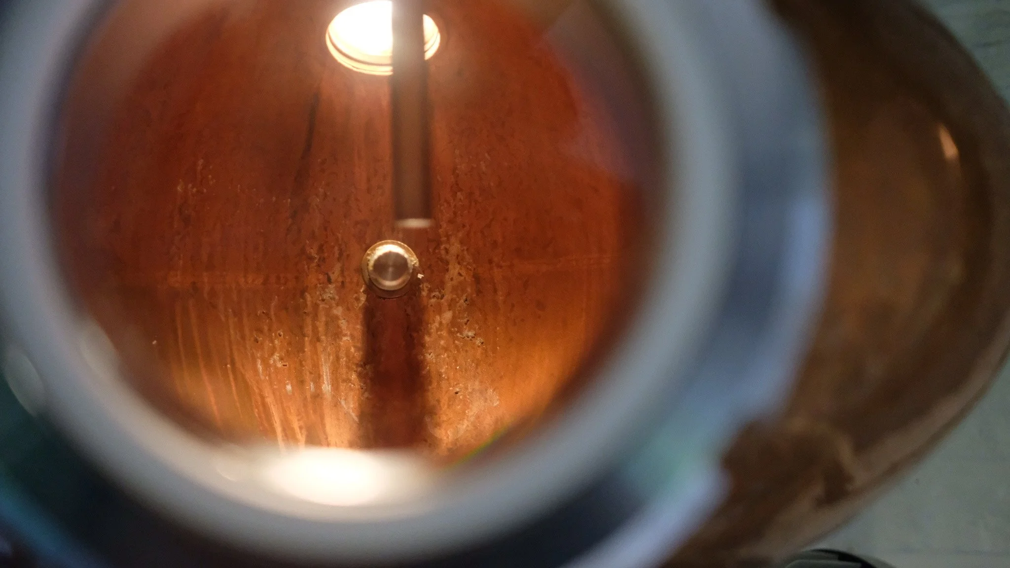 Vue à l'intérieur d'une bouteille en verre, révélant le fond en bois et un tube métallique au centre.