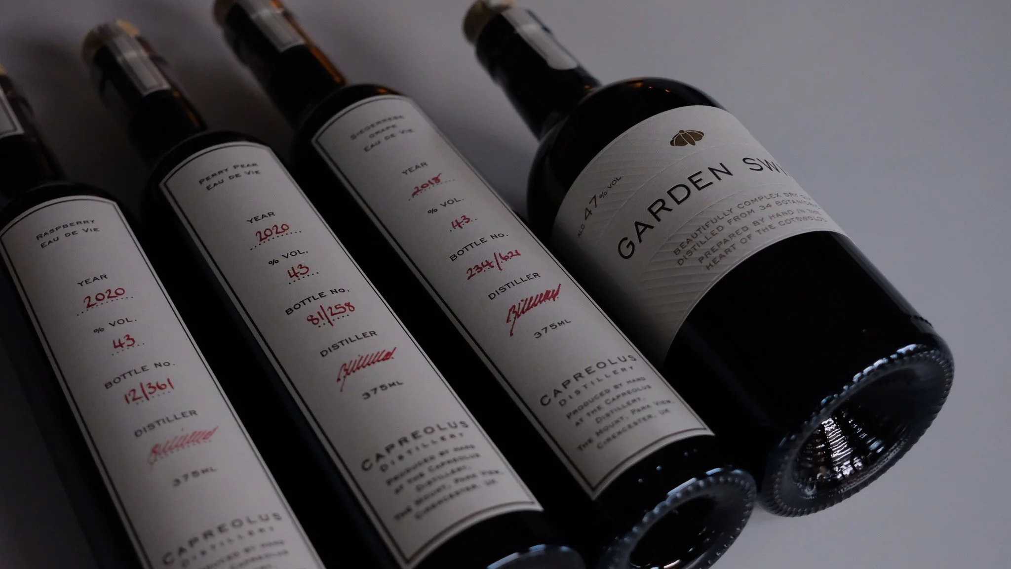 Quatre bouteilles de vin alignées, avec des étiquettes indiquant l'année, le volume et le nom du distillateur, sur fond blanc.