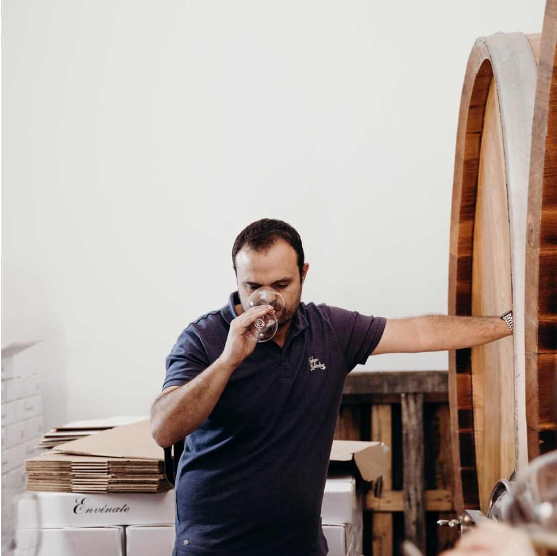 Un homme qui sent un verre de vin dans une cave ou un espace de stockage de vin, les bras tendus.