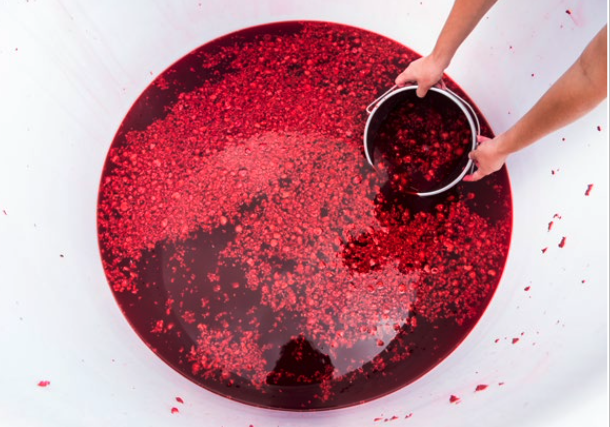 Person versant du liquide rouge avec des morceaux de confettis dans un grand bol.