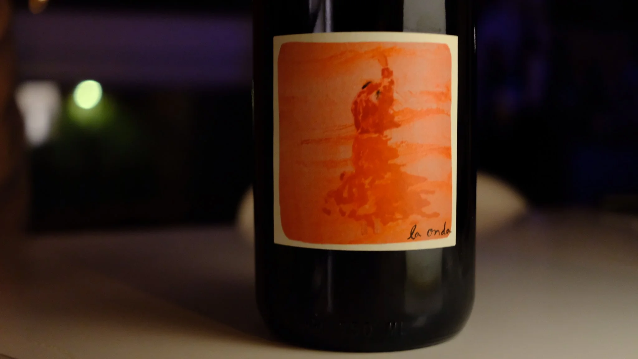 Bouteille de vin avec une étiquette orange représentant une silhouette de femme sur fond orange, avec le texte "la onda" en bas à droite.