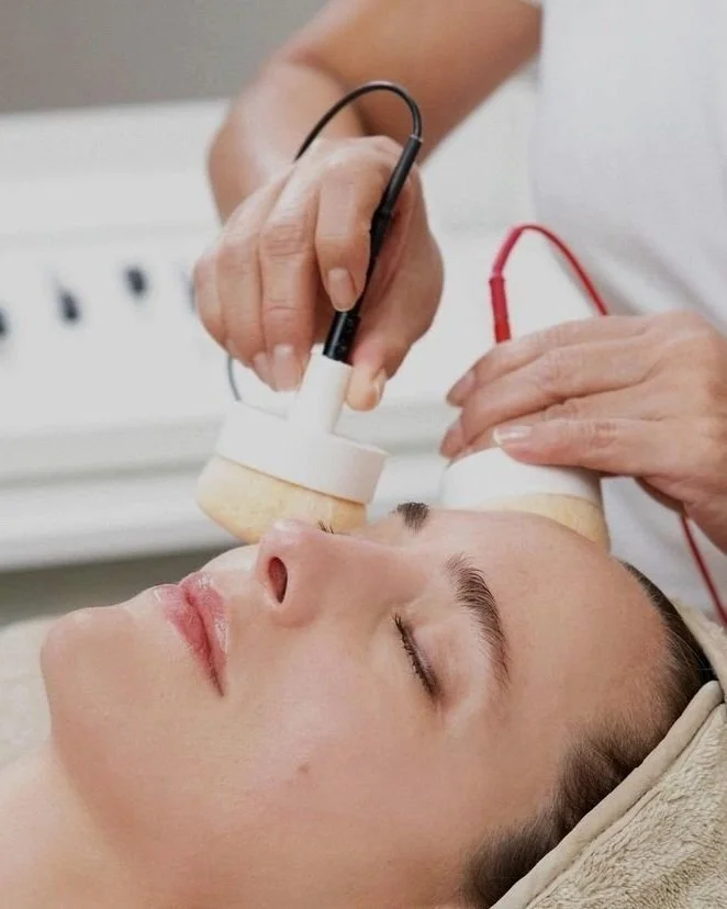 A person receiving a facial treatment with a device held by an aesthetician in a skincare clinic.