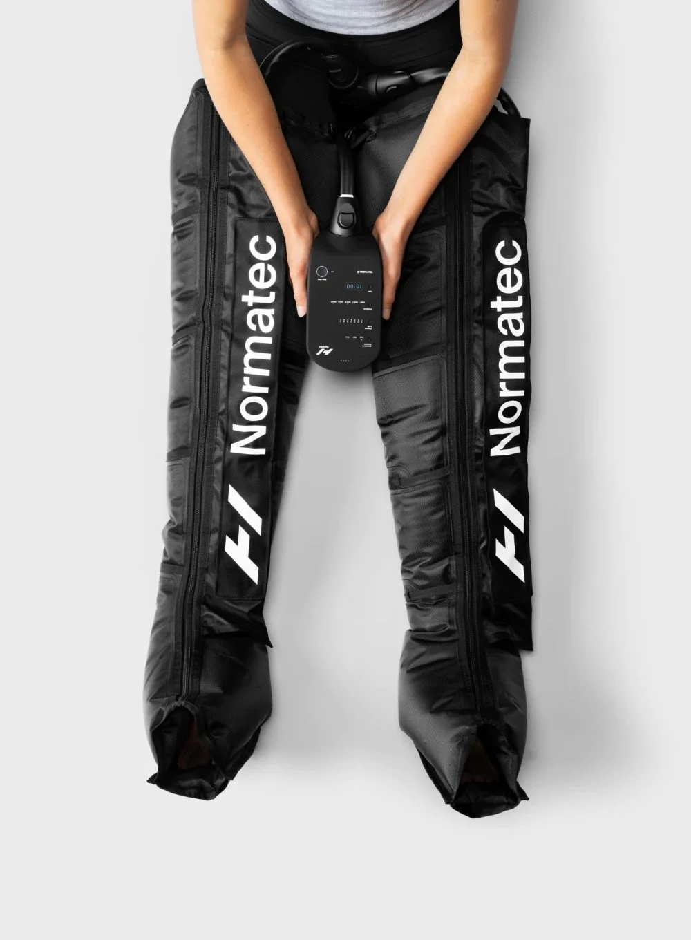 Person holding a control device while sitting on a large black Nordmatec branded bag or gear with zippers, against a white background.