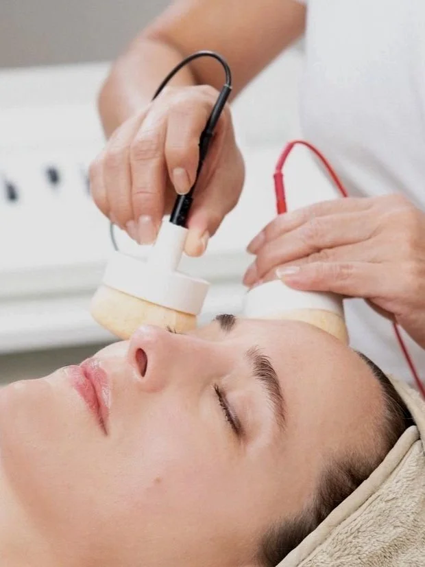 A woman lying with her eyes closed while a healthcare professional uses ultrasound equipment on her face.
