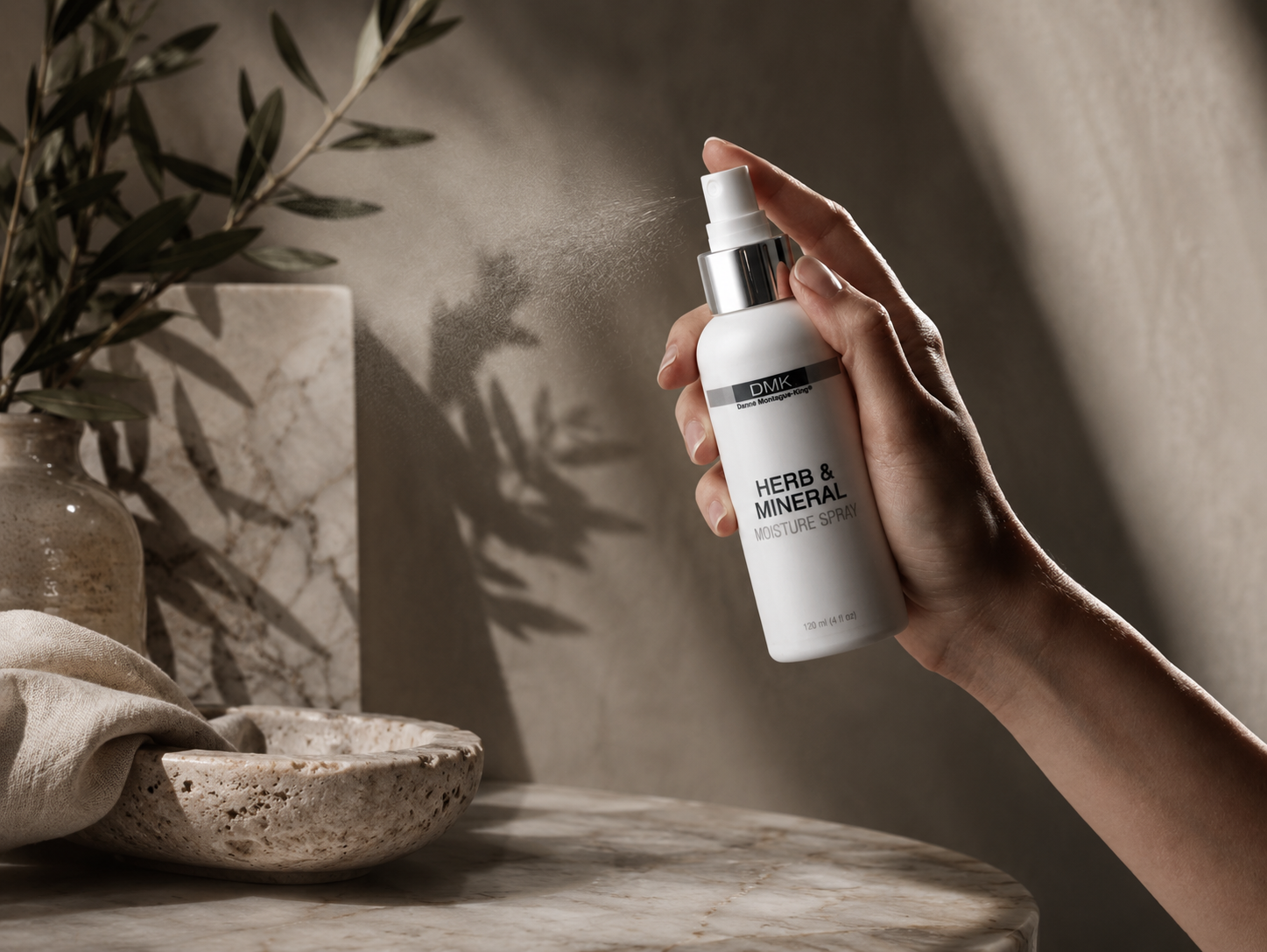 A hand holding a metallic copper-colored bottle of Augstinous Bader eye cream with some cream on the back of the hand.