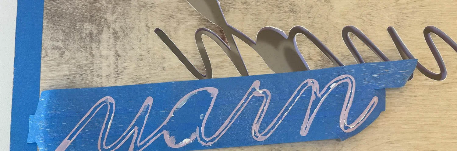closeup detail of blue painters tape with purple paint tracing the word yarn