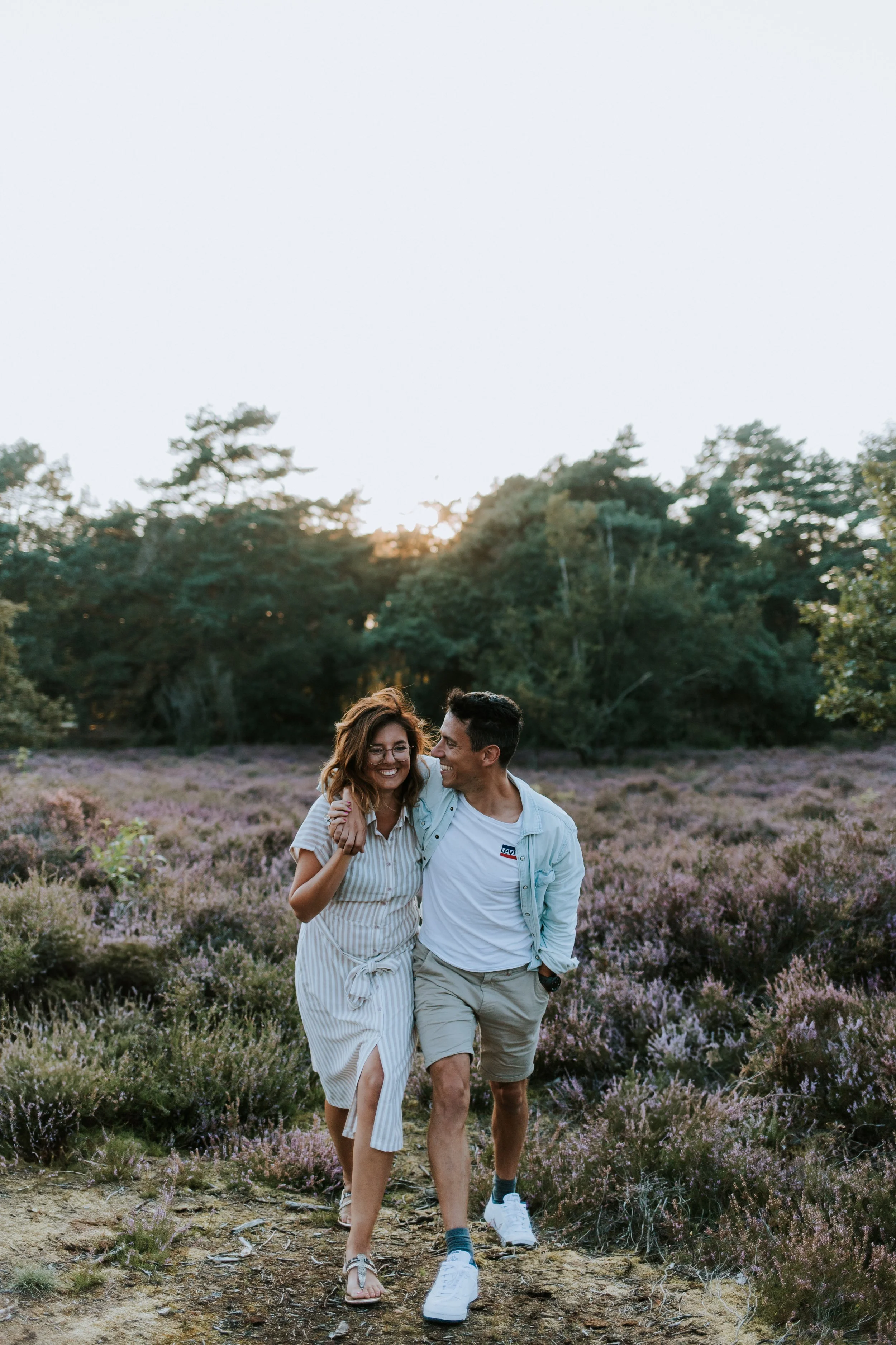 Koppel wandelt hand in hand tussen de heide tijdens de zonsondergang.
