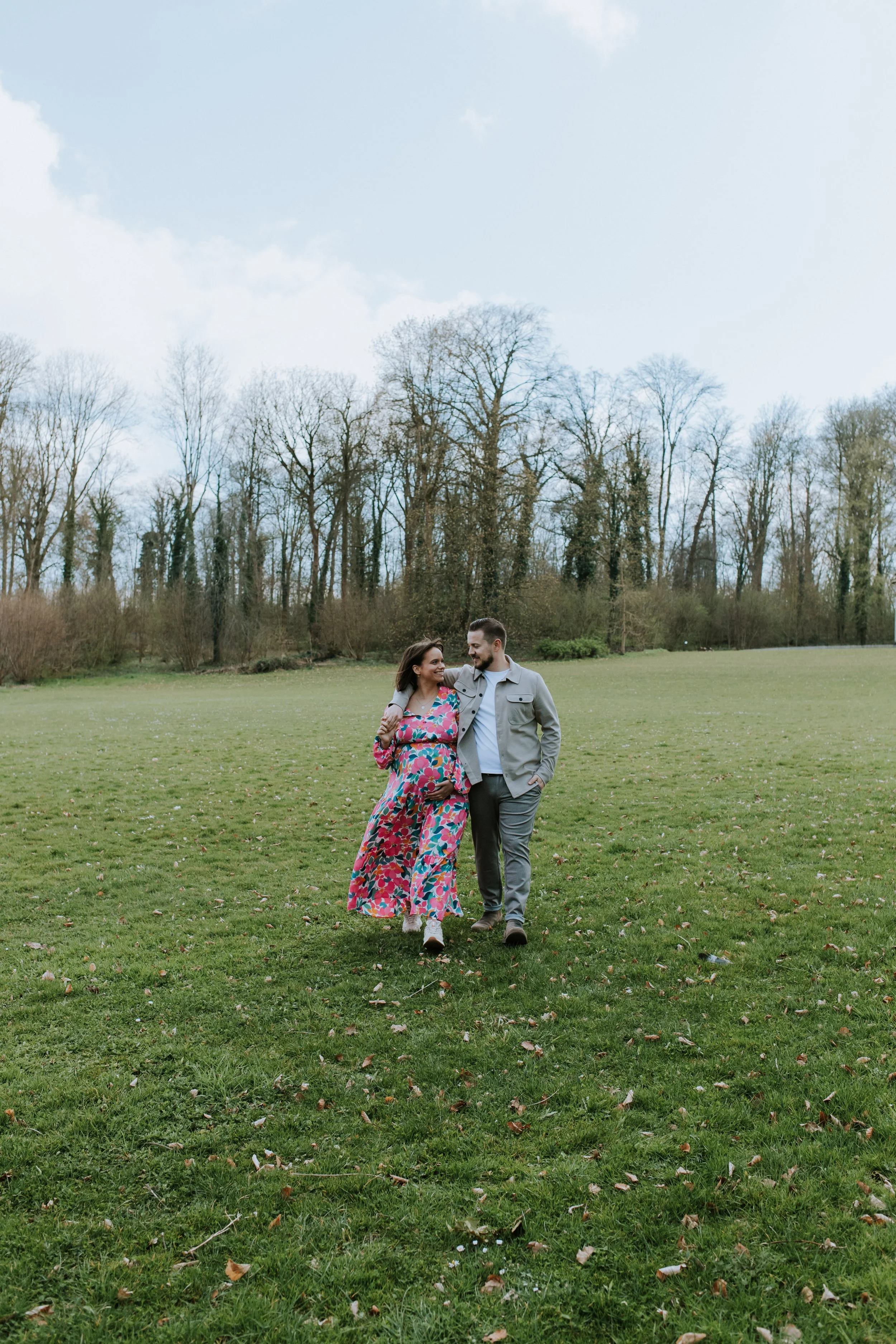 De toekomstige ouders wandelen hand in hand op een mooie groene veld tijdens de zwangerschapsshoot.