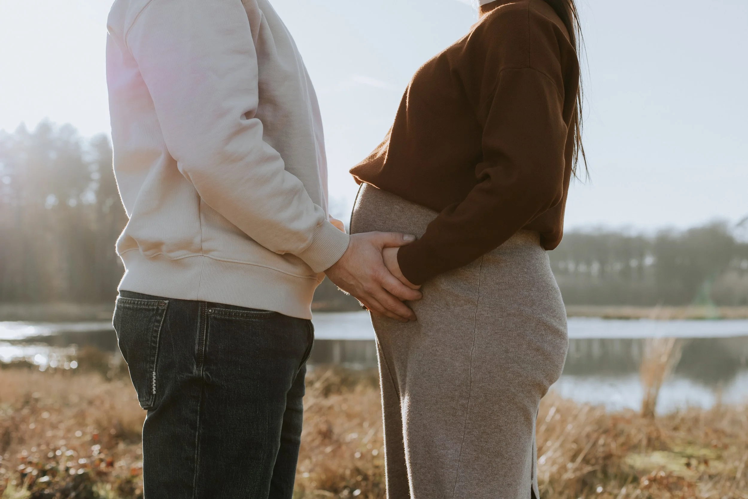 Mama en papa leggen beide hun handen op de bolle buik tijdens een zwangerschapsshoot.