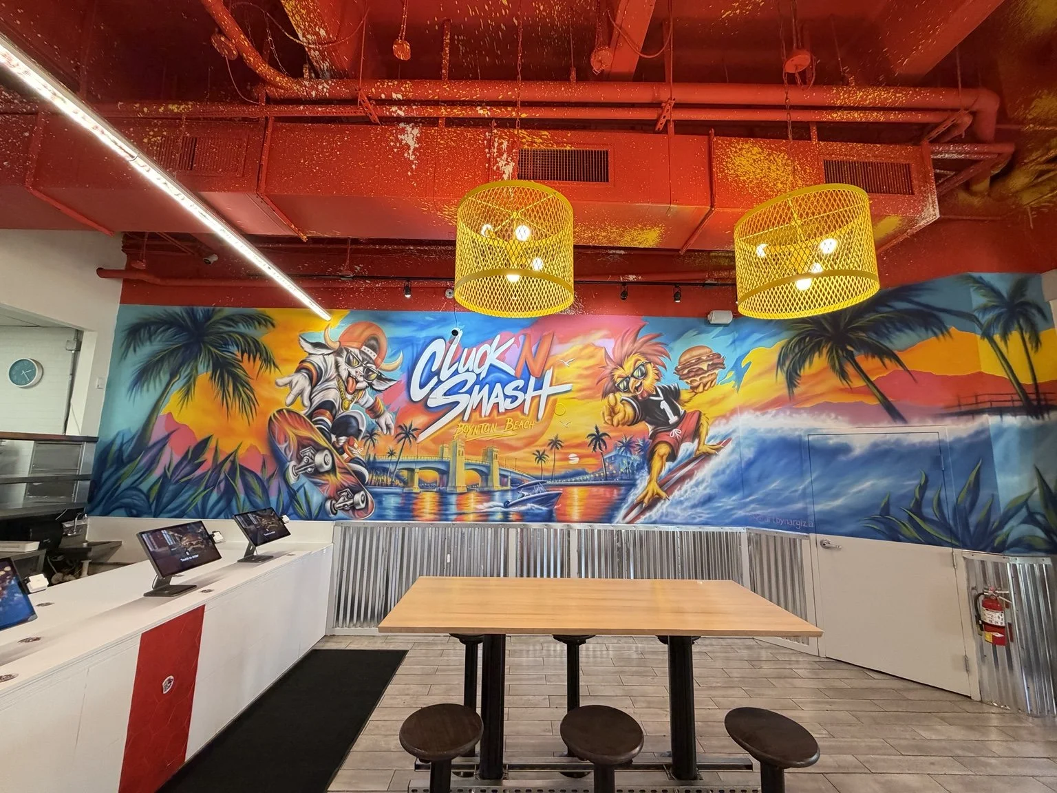 Wide interior view of the colorful Cluck N Smash mural and dining area in Boynton Beach