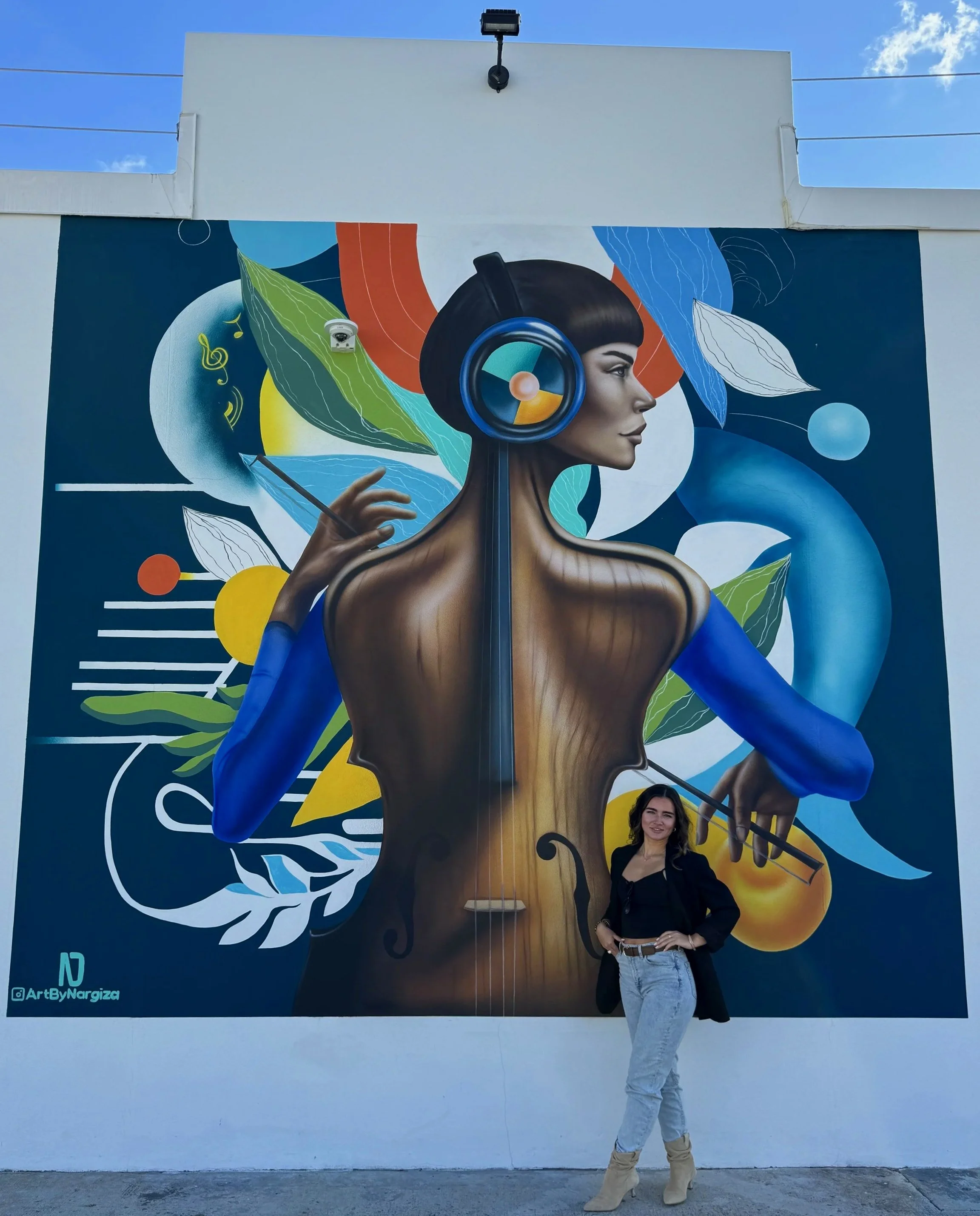 Mural artist Nargiza Dadabaeva standing with the completed Timeless Fusion mural