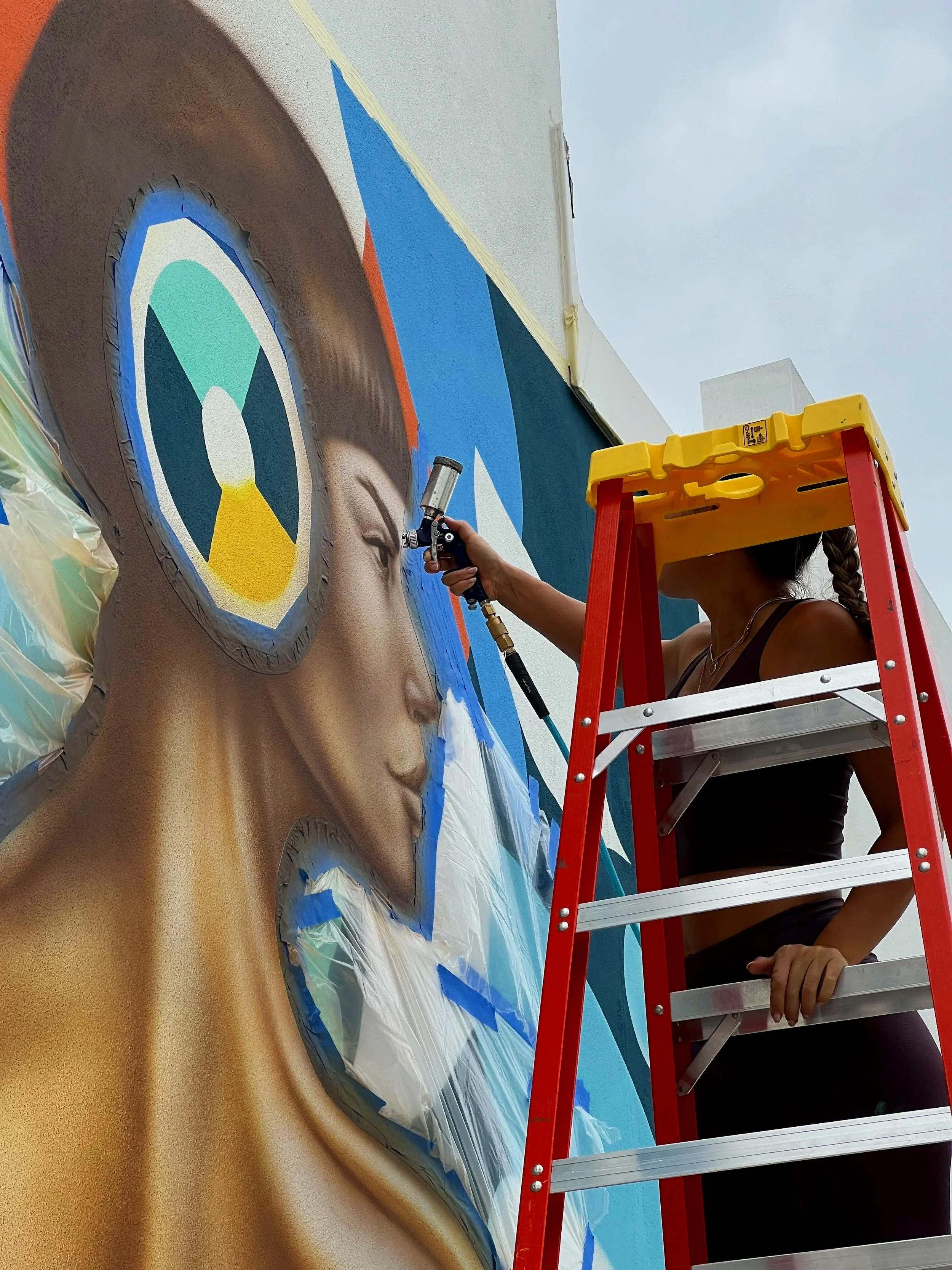 Nargiza Dadabaeva airbrushing the headphone and violin figure during the mural process