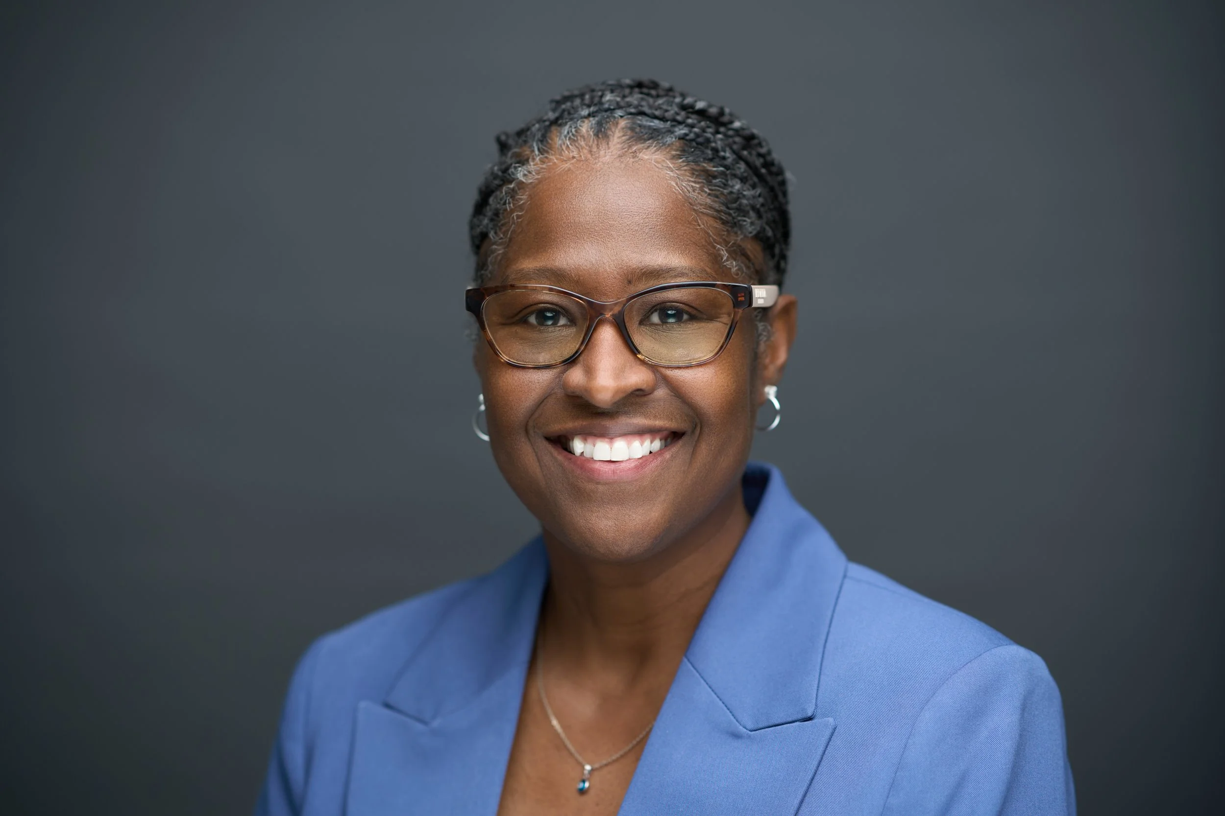 Smiling person in a plaid blazer against a gray background